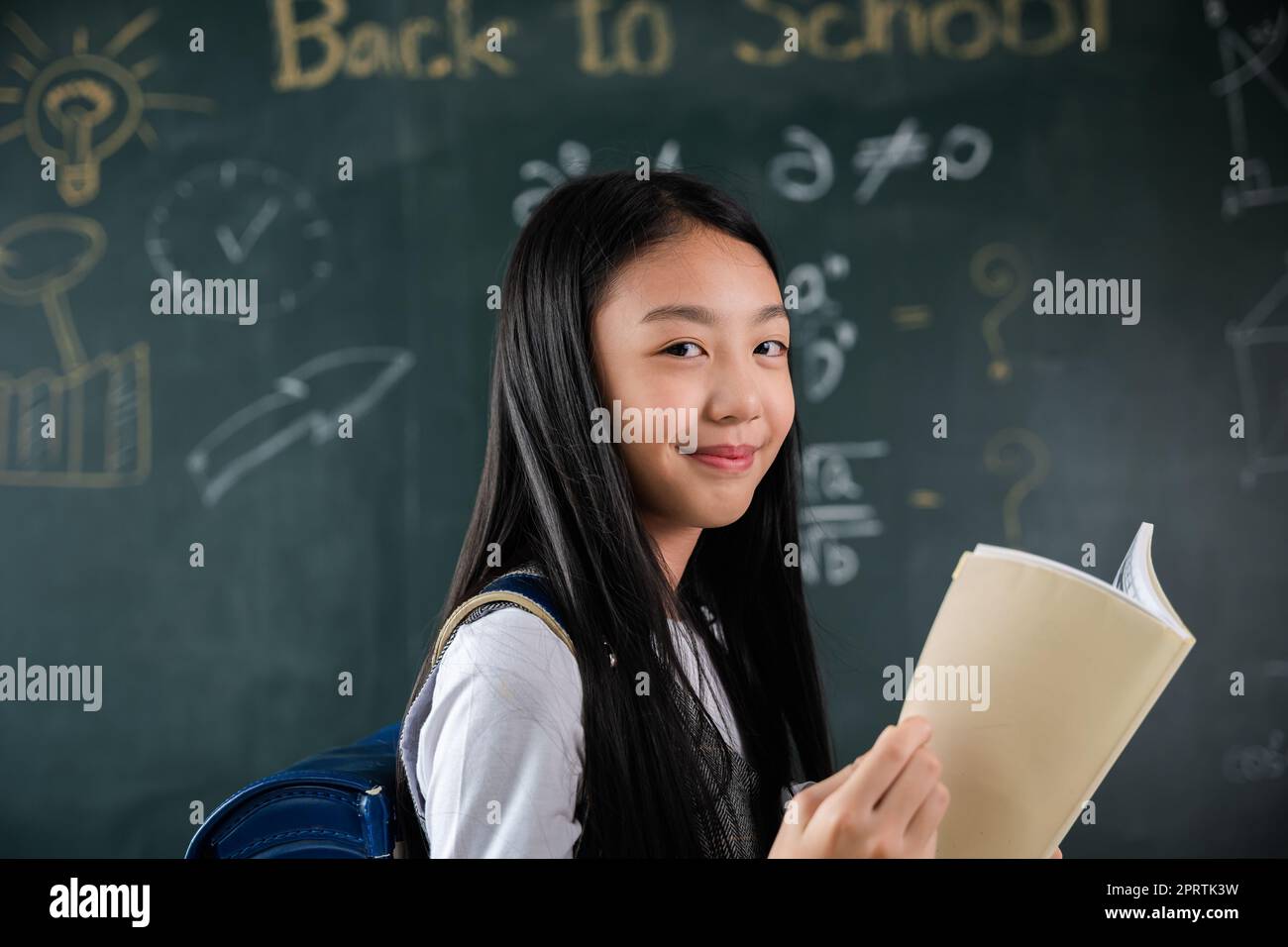 Heureuse belle fille d'école asiatique debout tenant des livres debout devant le tableau noir de la salle de classe Banque D'Images