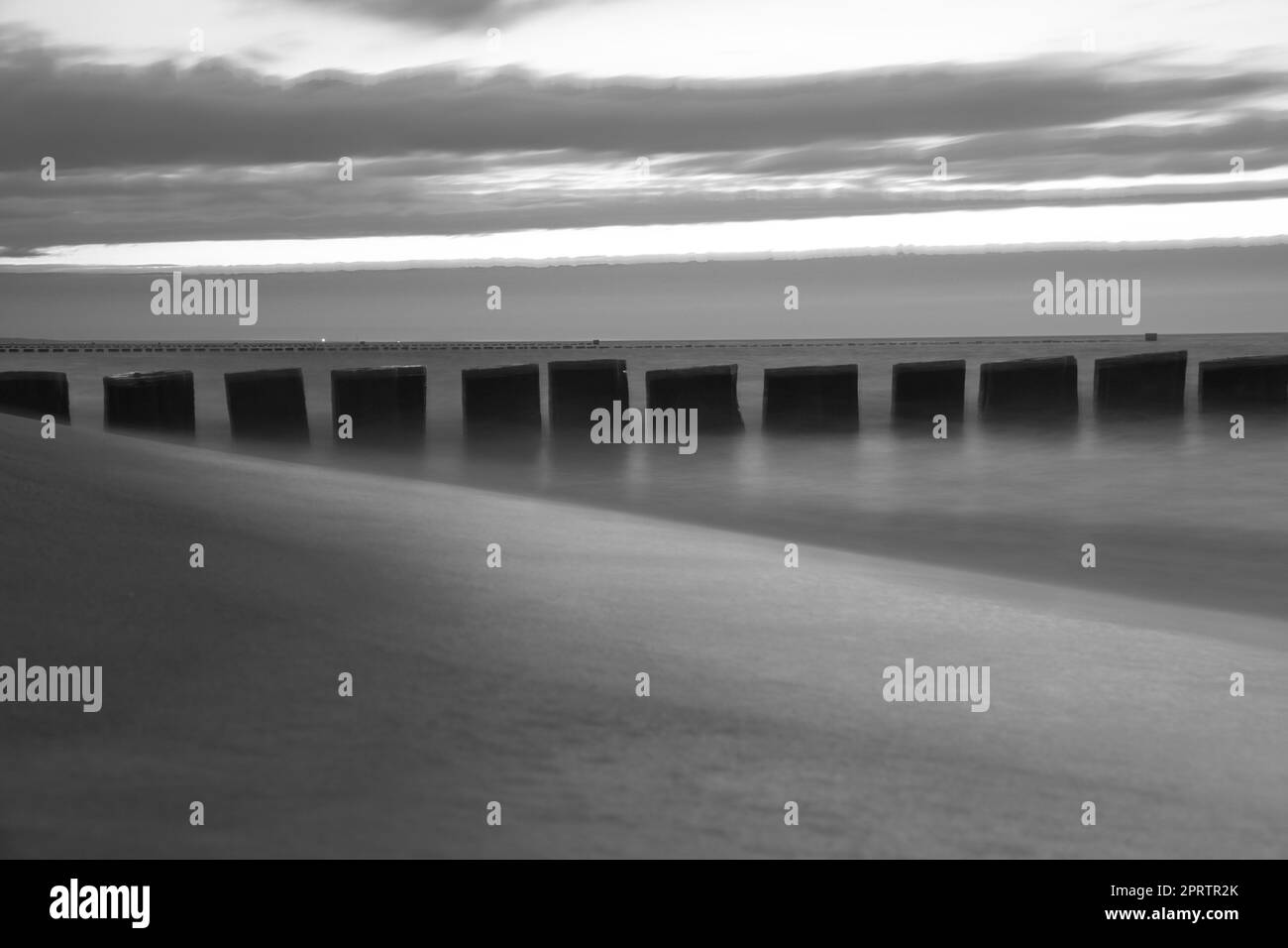 Coucher de soleil en noir et blanc sur la plage de la mer Baltique. Les groynes dépassent dans la mer Banque D'Images