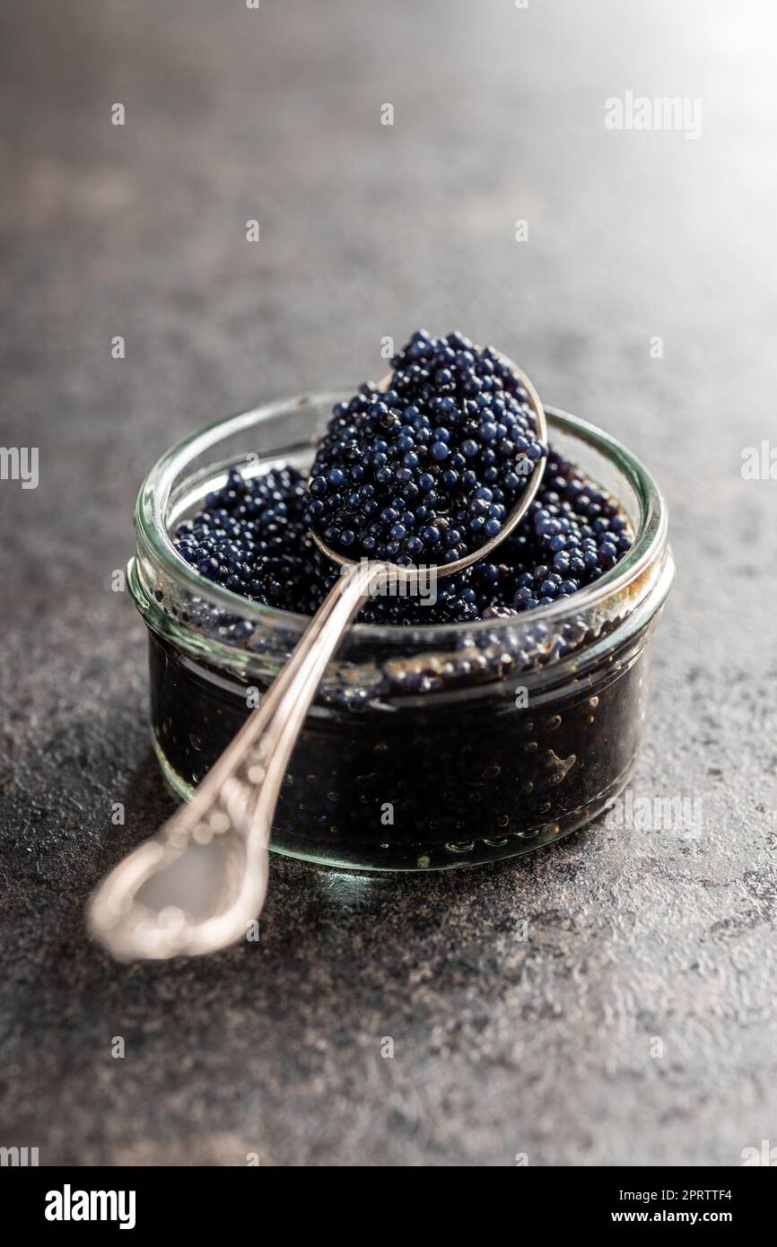 Caviar noir dans une cuillère argentée sur une table sombre. Banque D'Images
