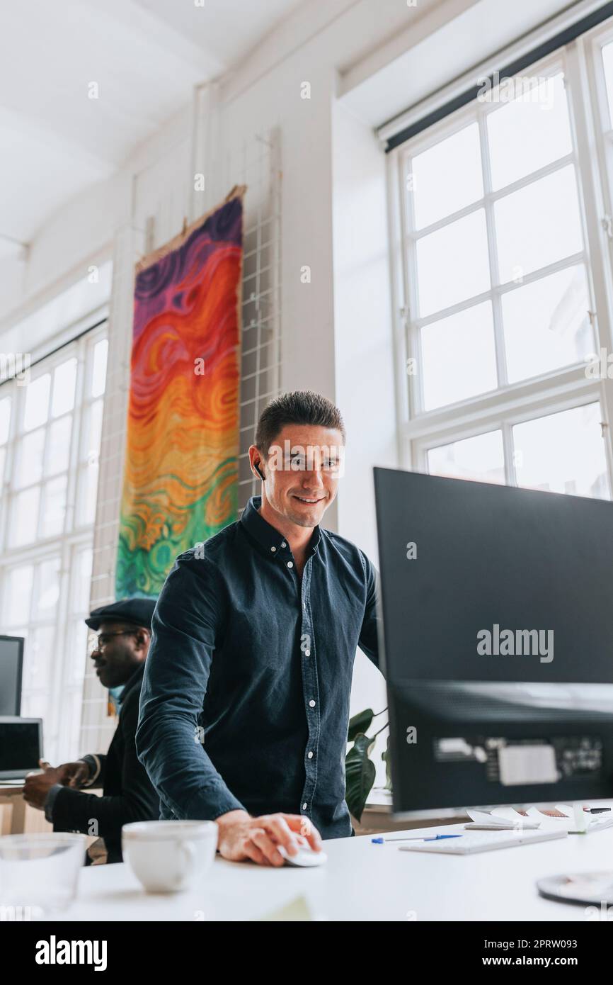 Jeune homme d'affaires souriant utilisant un PC de bureau au bureau Banque D'Images