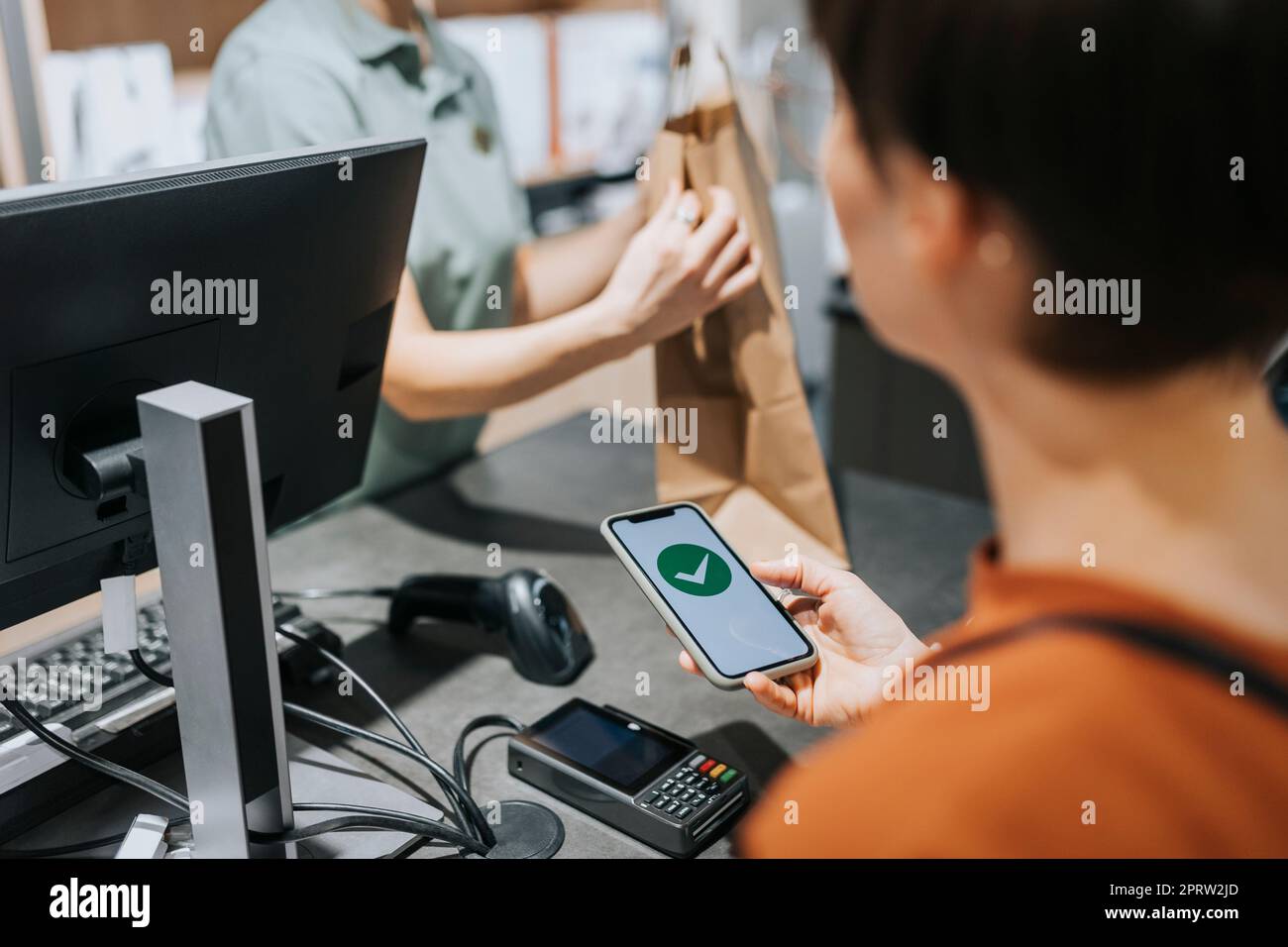 Une cliente qui scanne un lecteur de carte de crédit tout en payant par téléphone portable dans un magasin d'électronique Banque D'Images