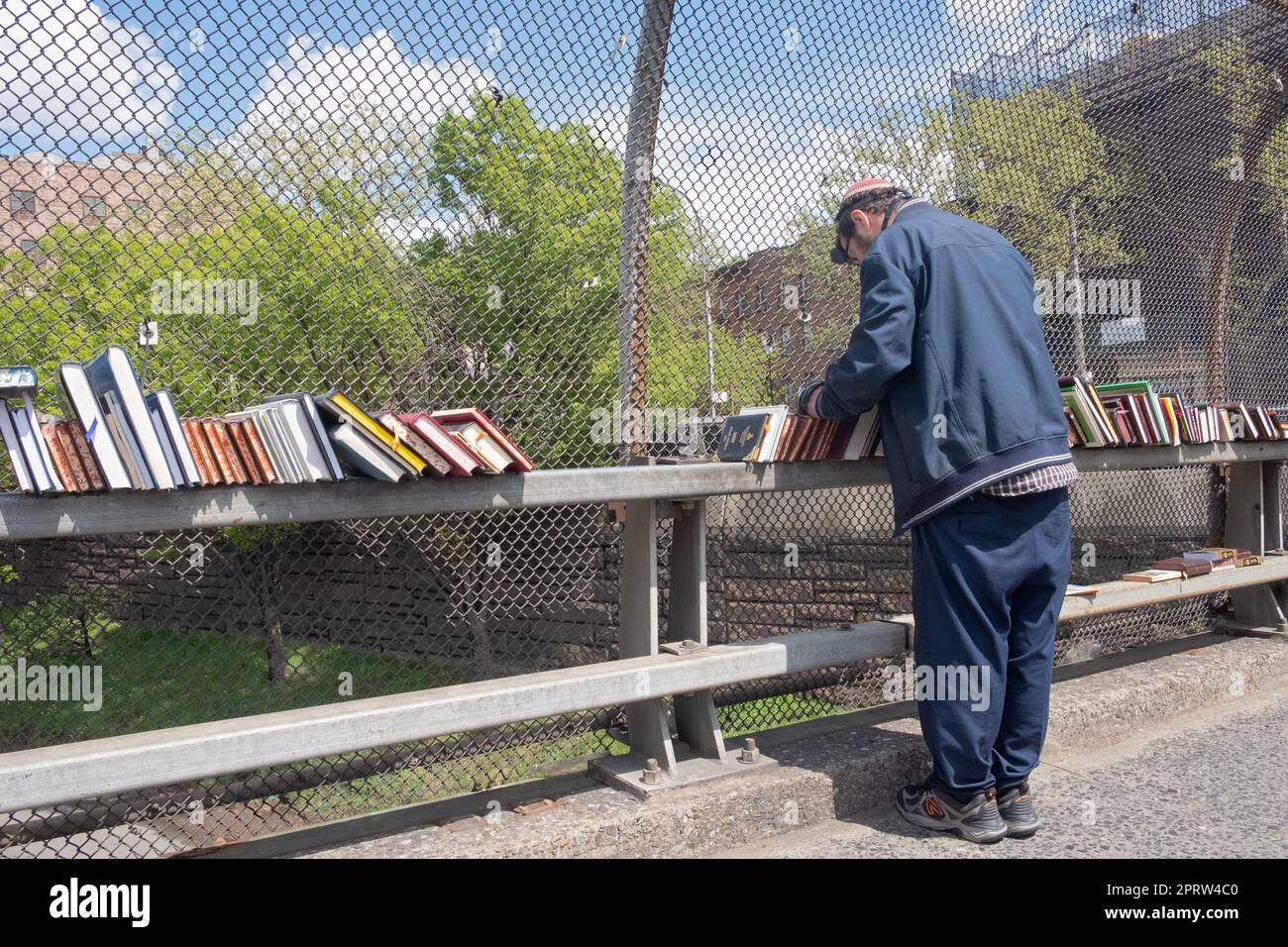 Un juif orthodoxe qui vend des livres religieux récite ses prières du matin tout en portant la téfiline (phylactères). Vue sur le BQE à New York. Banque D'Images