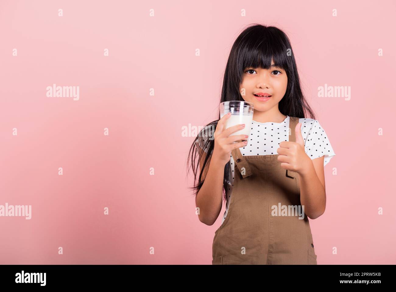 Petit enfant asiatique 10 ans sourire tenir le verre de lait boire du lait blanc et montrer le pouce vers le haut du doigt pour le bon signe Banque D'Images