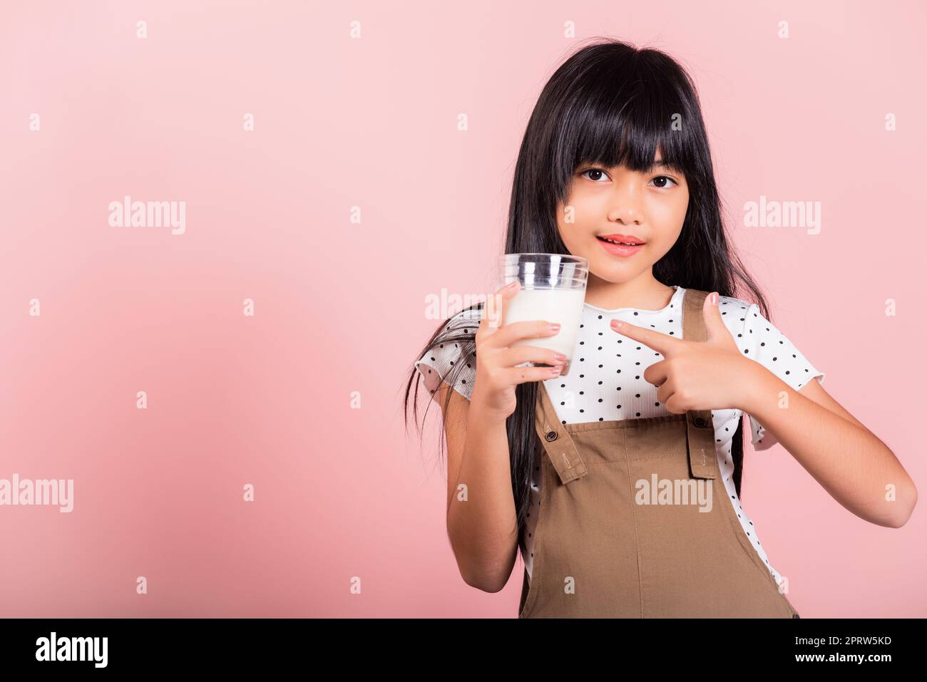 Petit enfant asiatique 10 ans sourire tenir le verre de lait boire du lait blanc et le doigt pointant Banque D'Images