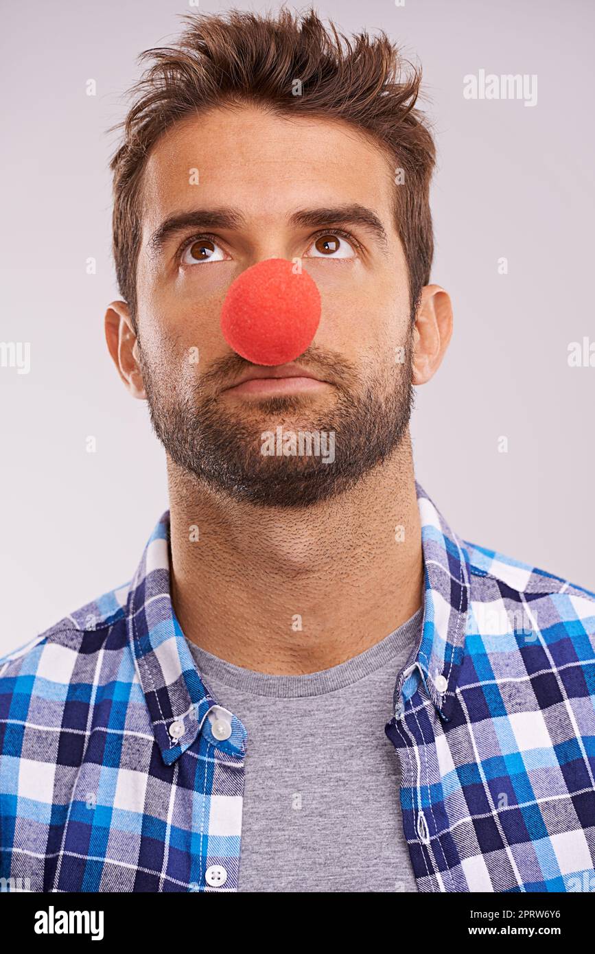 Se clowant. Photo studio d'un beau homme portant un nez rouge sur fond gris. Banque D'Images