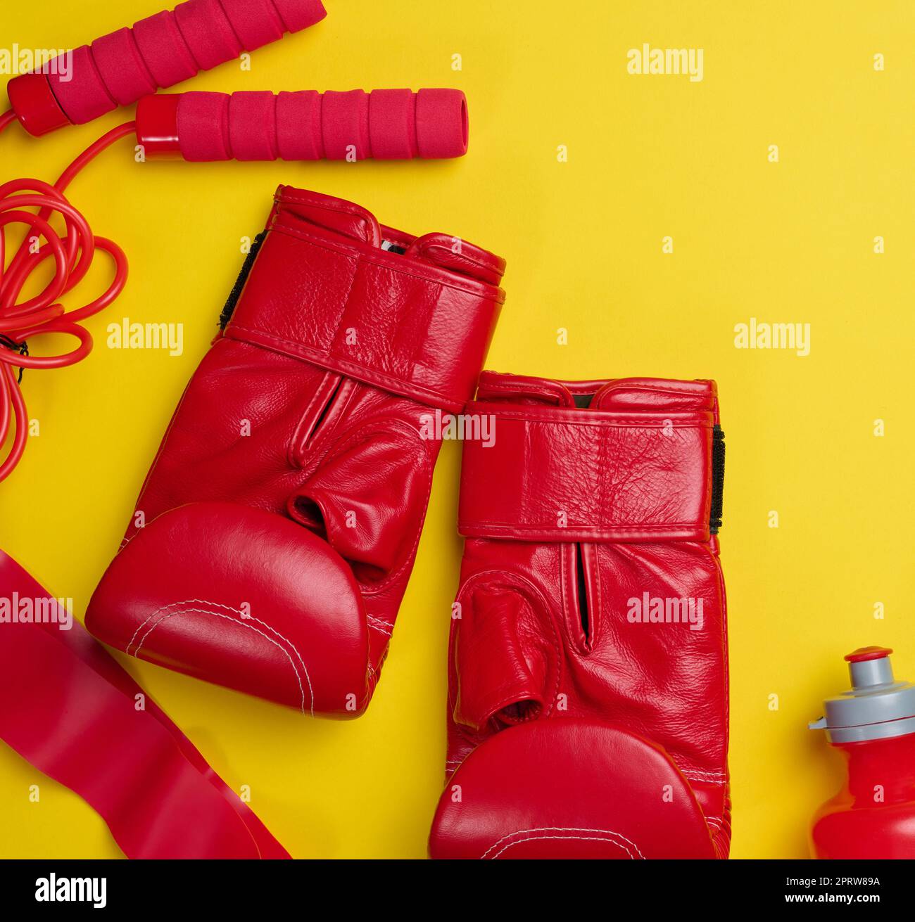 Gants de boxe en cuir rouge, bouteille d'eau. Équipement sportif sur fond jaune Banque D'Images