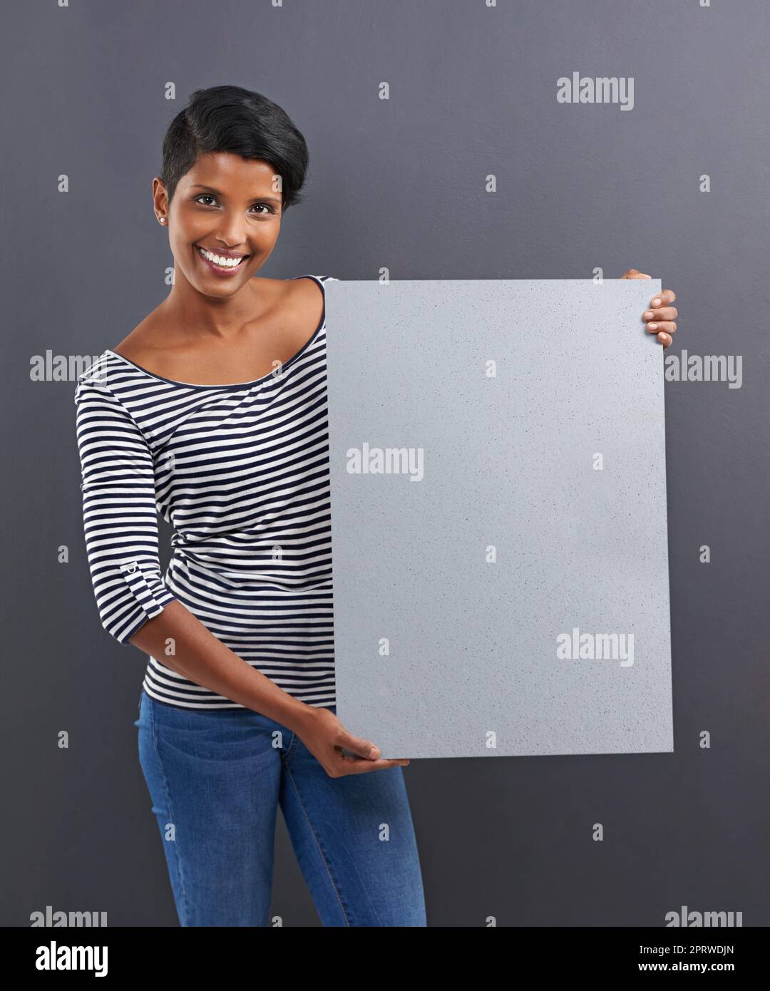 C'est VOTRE espace. Photo studio d'une belle jeune femme tenant un écriteau vierge sur fond gris. Banque D'Images