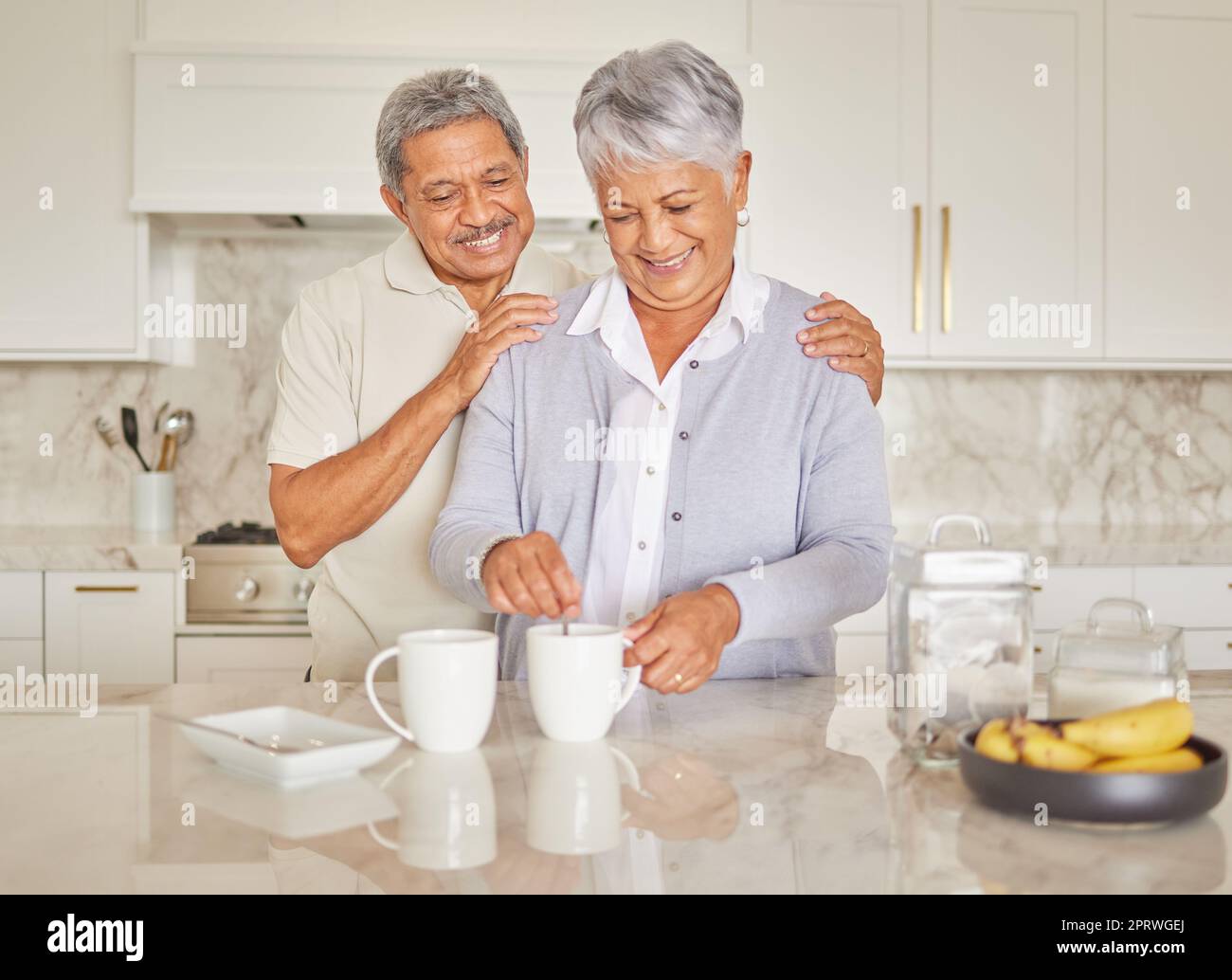 Le café, le couple et l'amour avec une femme et un homme âgés qui profitent de la retraite pendant qu'ils sont ensemble dans la cuisine de leur maison. Heureux, sourire et romance avec un homme et une femme retraités âgés qui font du thé Banque D'Images