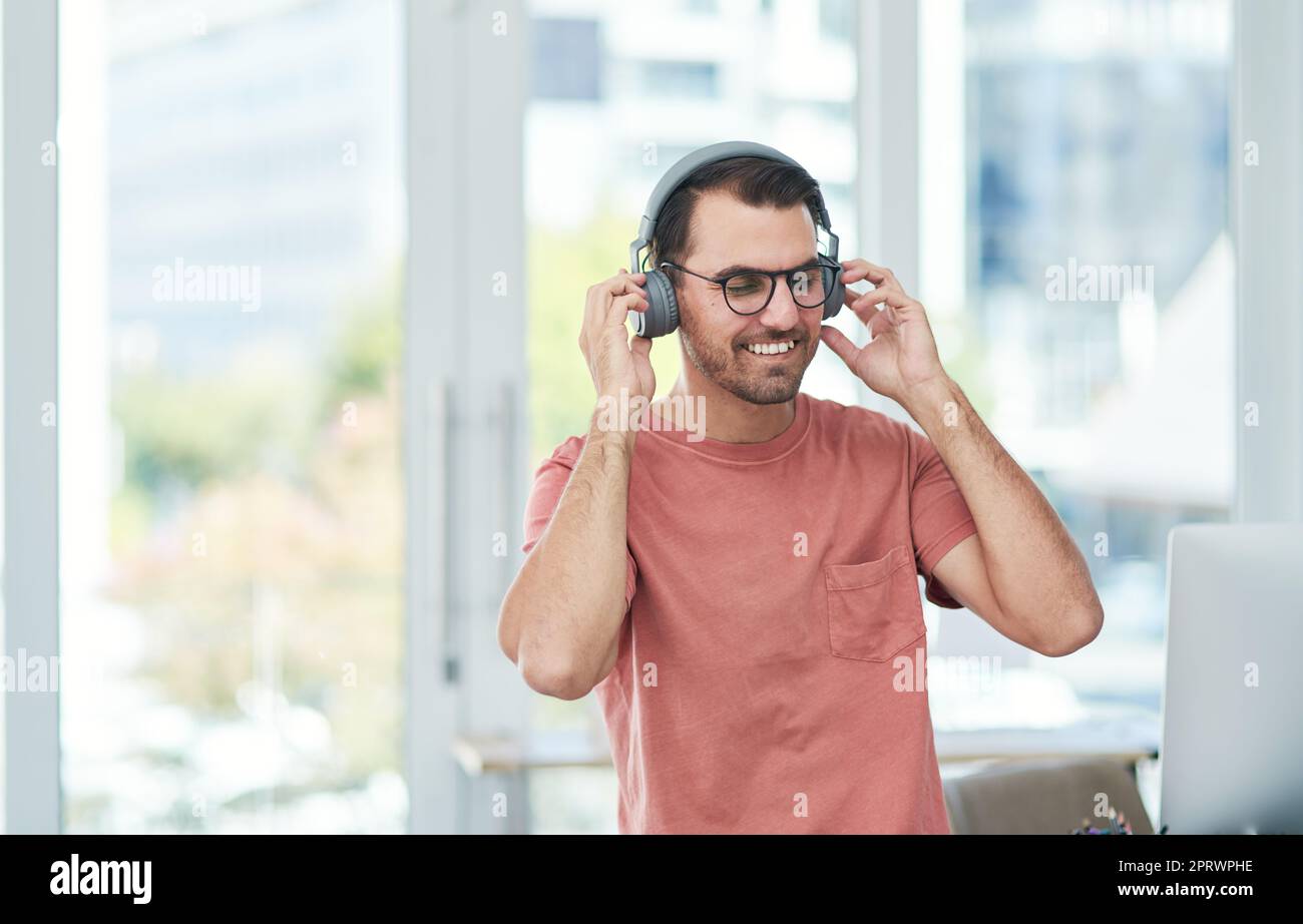 Faites une pause, mettez le rythme. Un jeune homme d'affaires heureux utilisant des écouteurs dans un bureau moderne. Banque D'Images