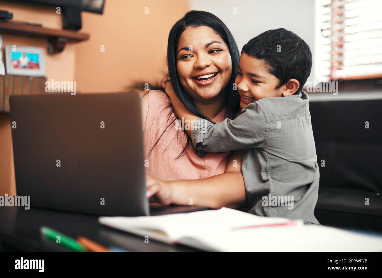 Chaque maman qui travaille est une superfemme. Une mère qui utilise un ordinateur portable alors que son fils l'embrasse à la maison. Banque D'Images