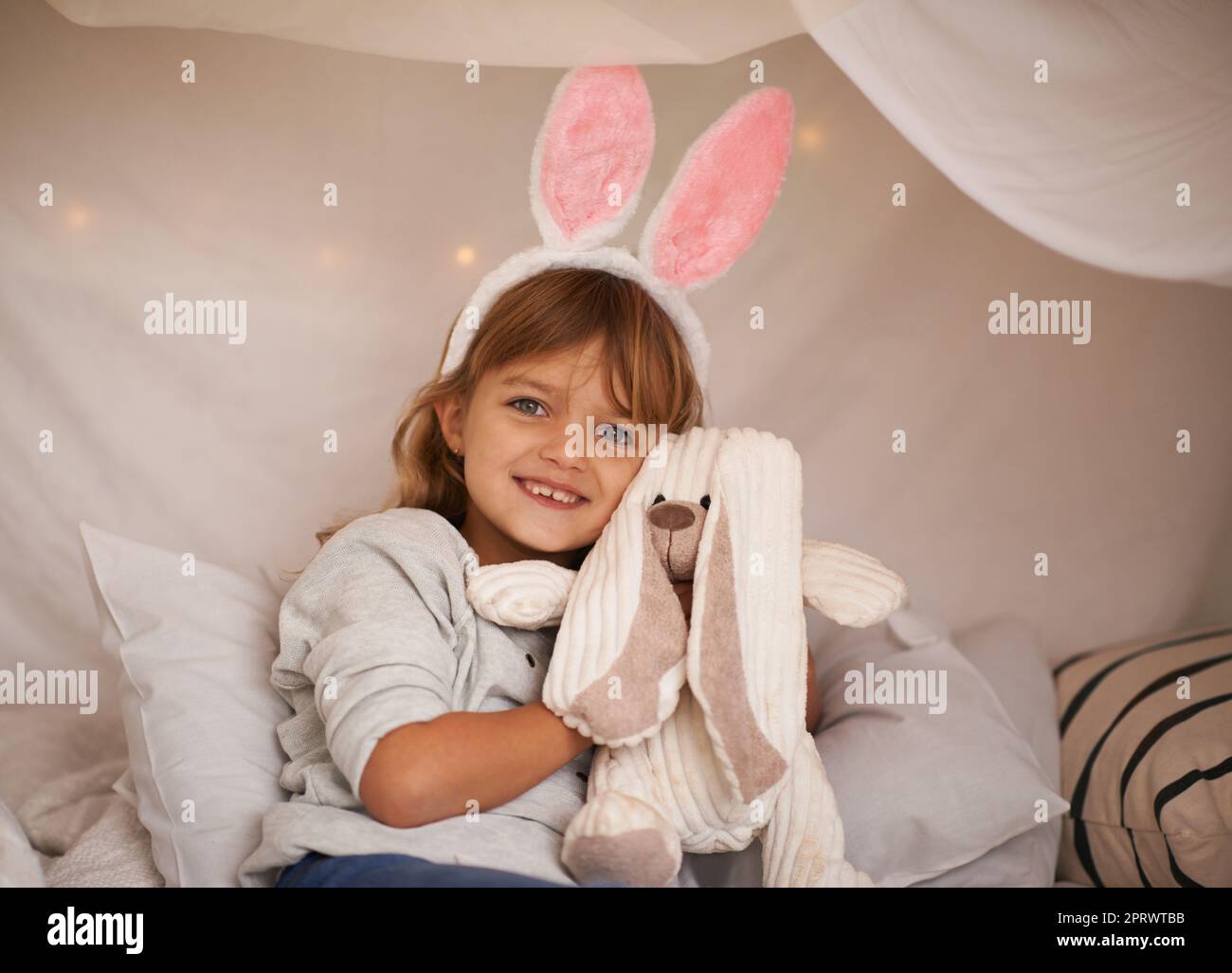 Apprendre à aimer. Portrait d'une adorable petite fille portant des oreilles de lapin et tenant son lapin jouet. Banque D'Images