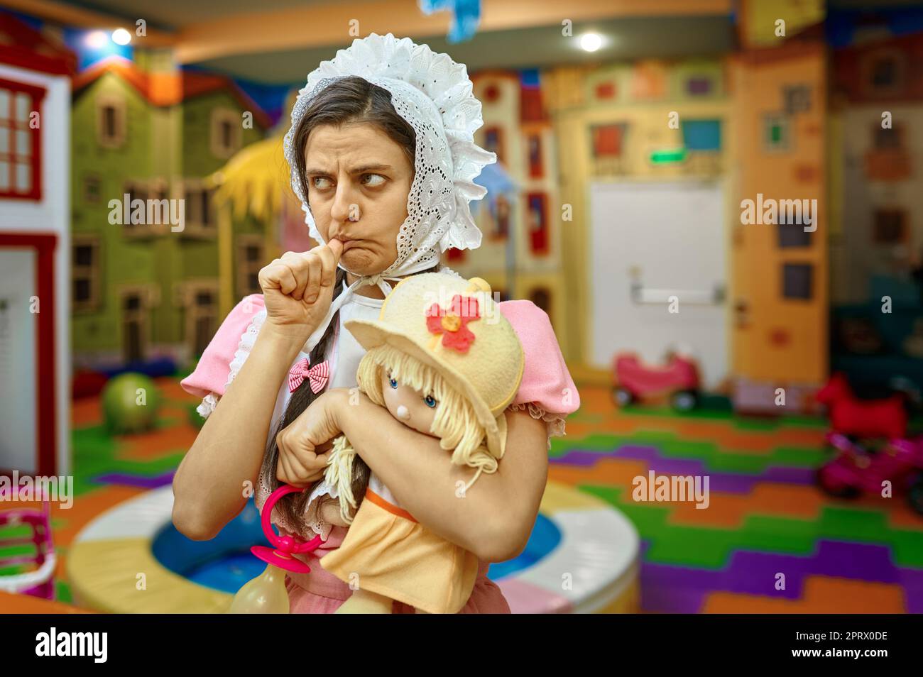 Adorable femme portant comme un nouveau-né enfant pouce suçant tenant jouet  poupée sur l'aire de jeux intérieure Photo Stock - Alamy
