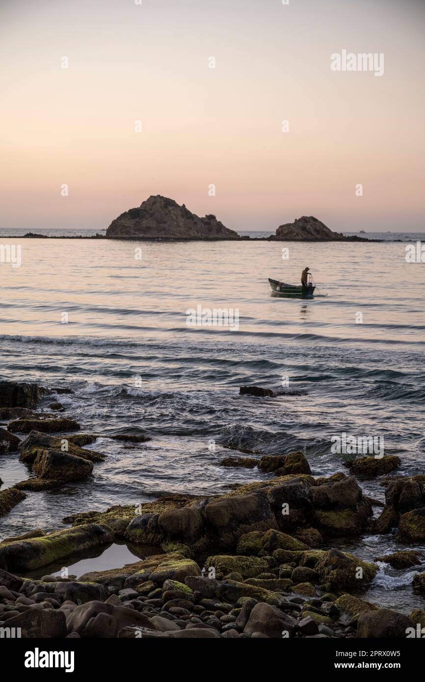 Silhouette d'un pêcheur se préparant à jeter les filets dans la mer au coucher du soleil. Banque D'Images
