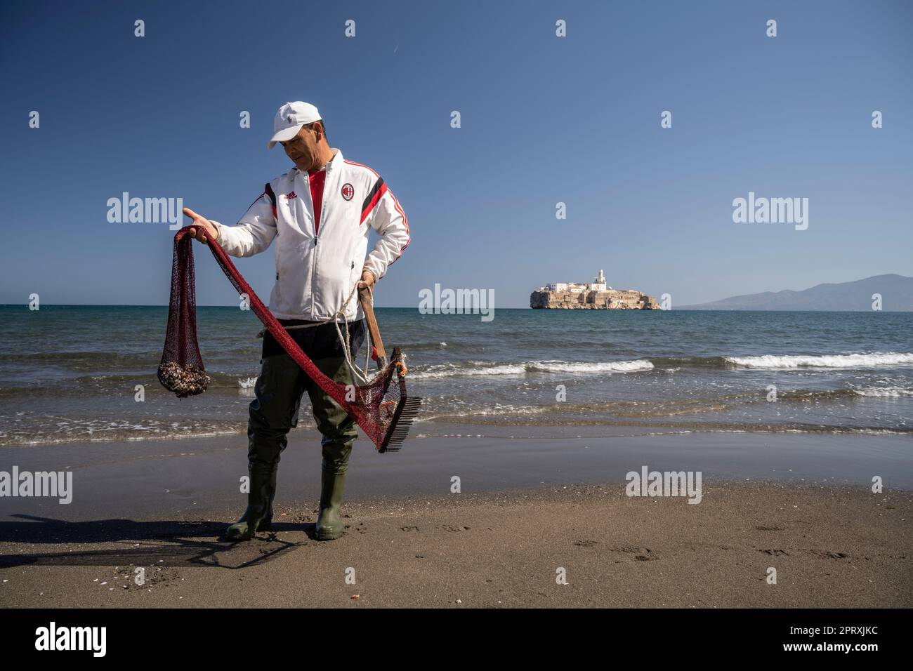 Homme collectant des coquillages sur la plage de Tayeth en face du Rocher d'Al Hoceima. L'île est le territoire espagnol au large de la côte du Maroc Banque D'Images