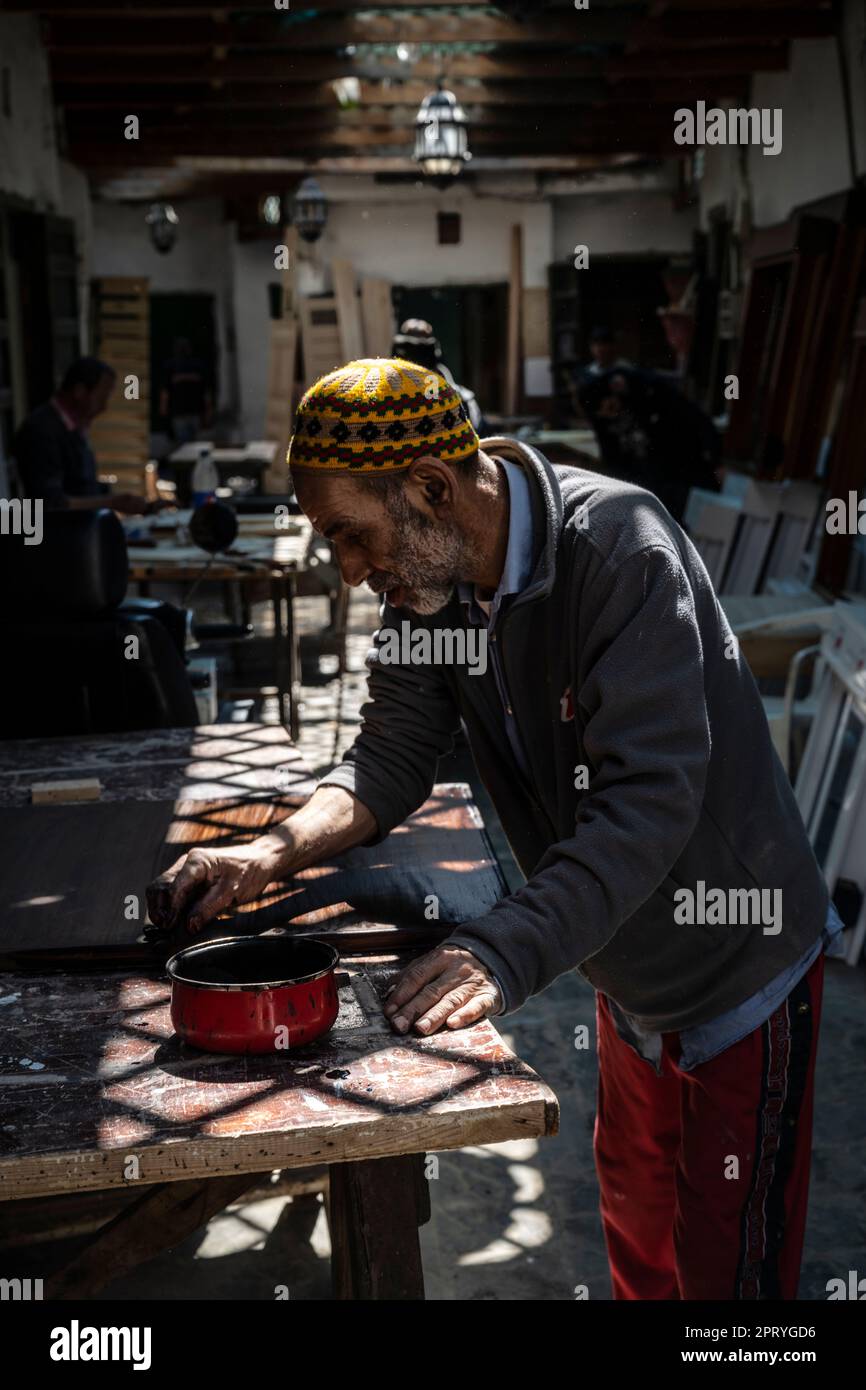 Carpenter vernis un morceau de bois à son poste de travail dans la médina de Tétouan. Banque D'Images