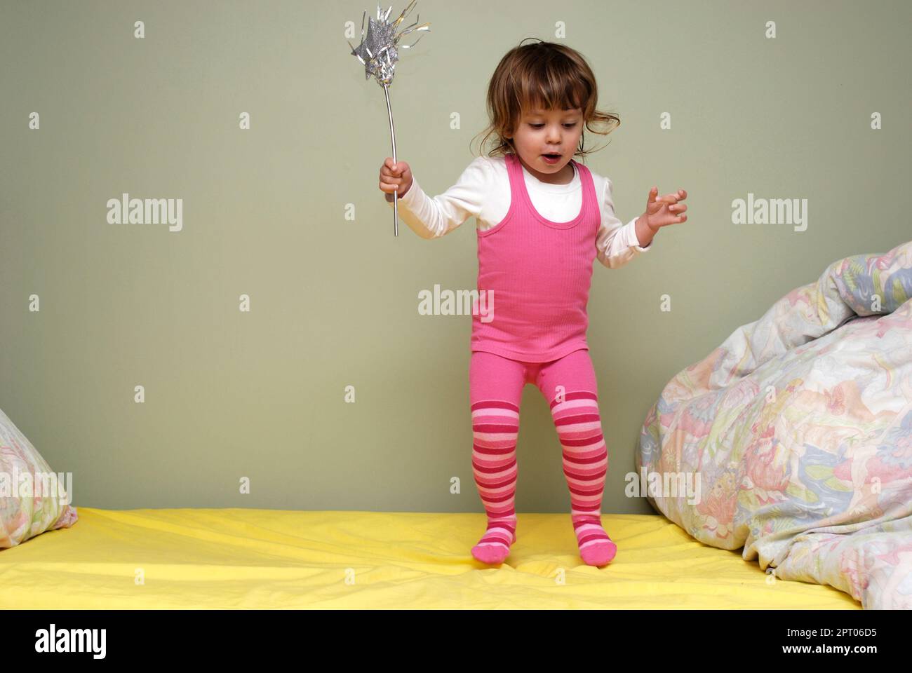 Un tout-petit heureux et enthousiaste tenant une baguette magique et rebondissant sur son lit. Banque D'Images