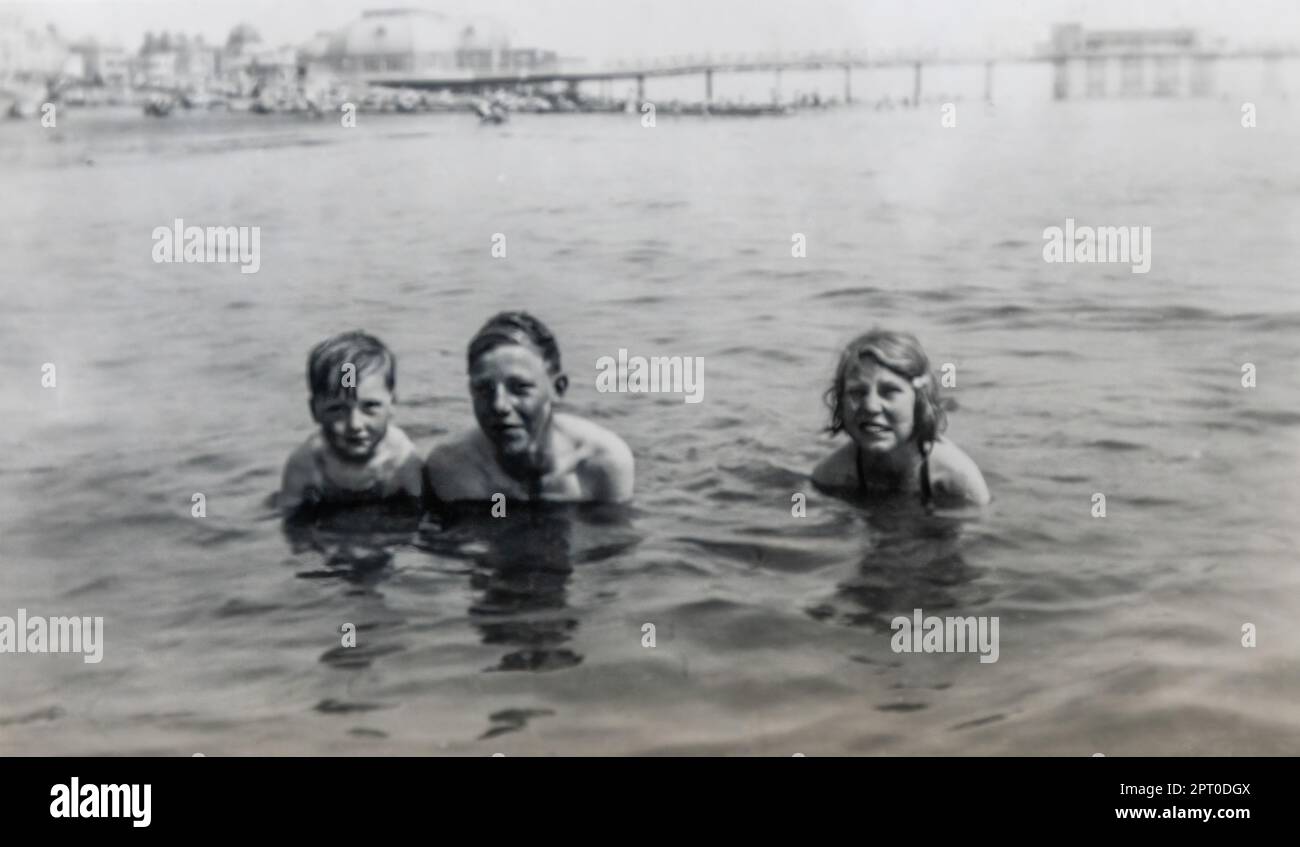 Enfants photographiés en mer lors d'un séjour en famille au bord de la mer avec un quai de plaisance en arrière-plan, photo d'archives en noir et blanc de la fin de 1940s Banque D'Images