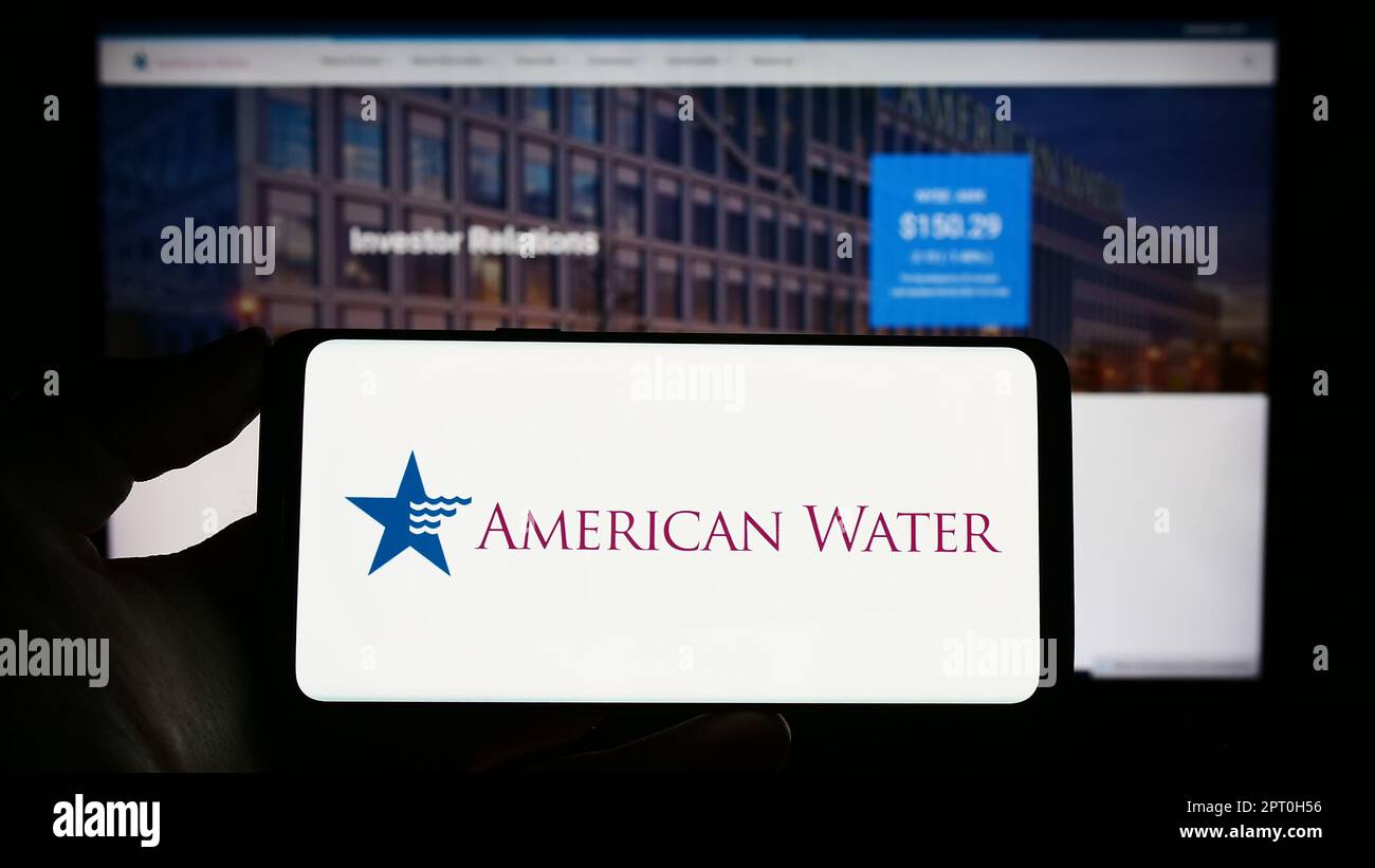 Personne tenant un téléphone cellulaire avec le logo d'American Water Works Company Inc. À l'écran devant la page Web d'affaires. Mise au point sur l'affichage du téléphone. Banque D'Images