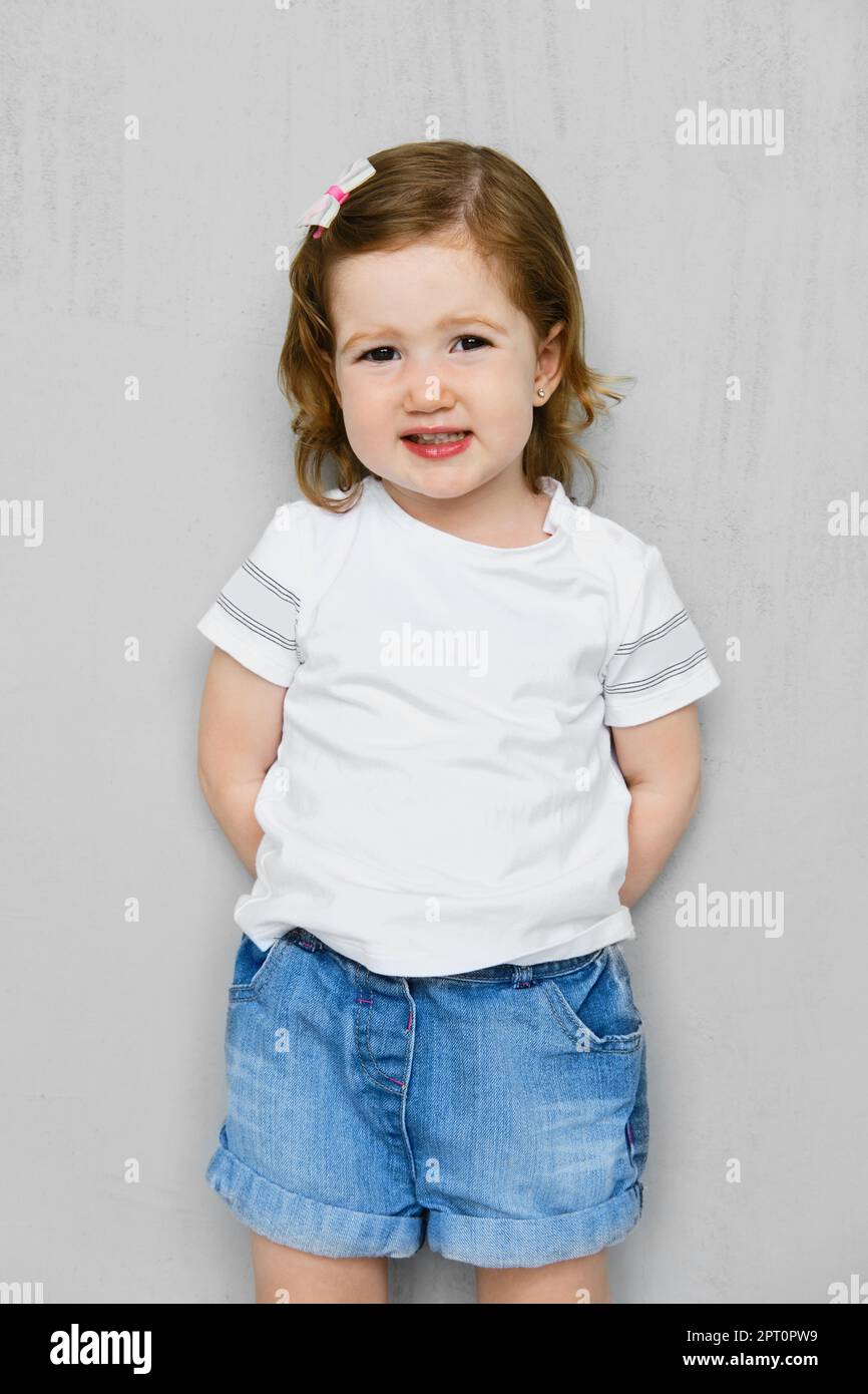 Fille de deux ans en t-short blanc et jeans short posant en studio Banque D'Images