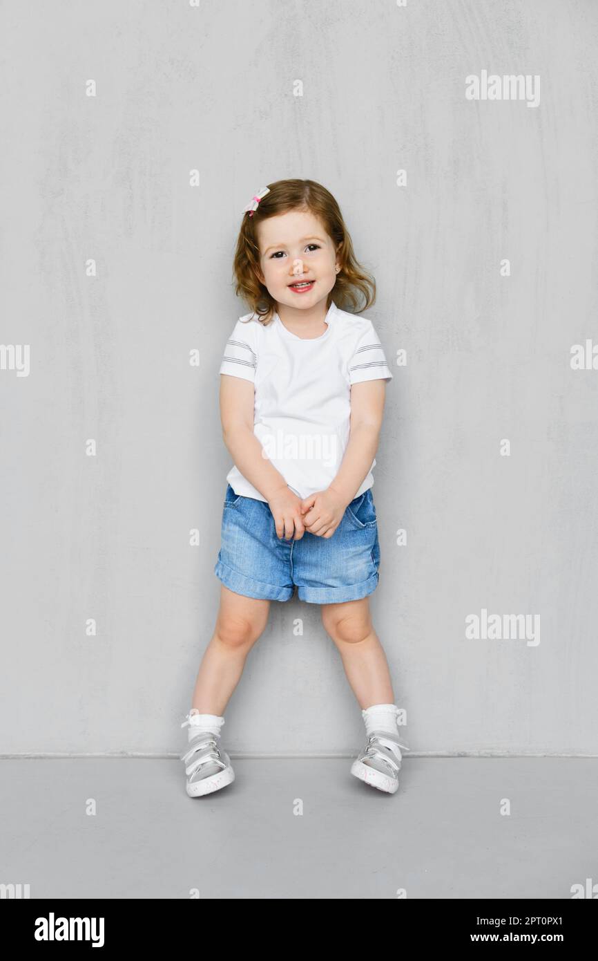 Fille de deux ans en t-short blanc et jeans short posant en studio Banque D'Images