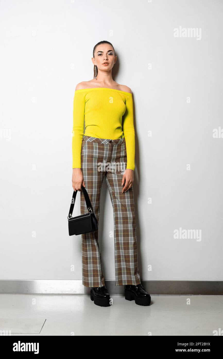 Fille en pantalon et pull jaune a carreaux avec petit sac a main posant pres de mur blanc Photo Stock Alamy