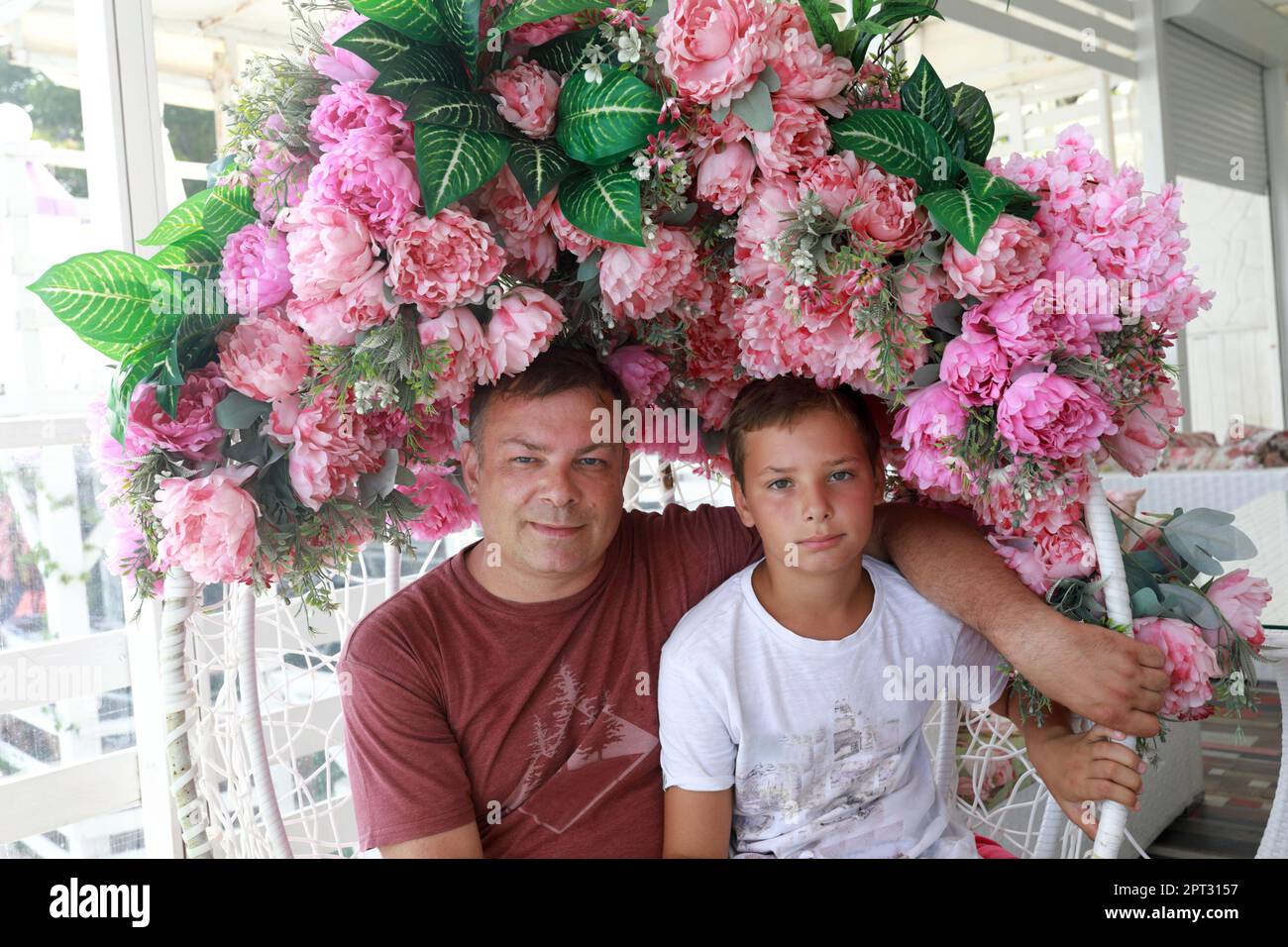 Père avec son fils posant dans un fauteuil suspendu décoré de fleurs Banque D'Images