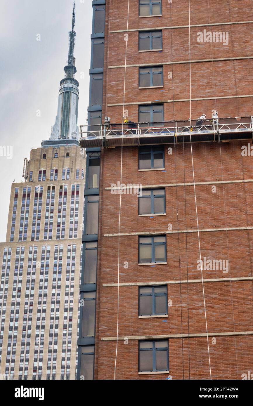 Les travailleurs effectuent un repointage de briques sur une plate-forme suspendue avec l'Empire State Building en arrière-plan, 2023, New York City, États-Unis Banque D'Images