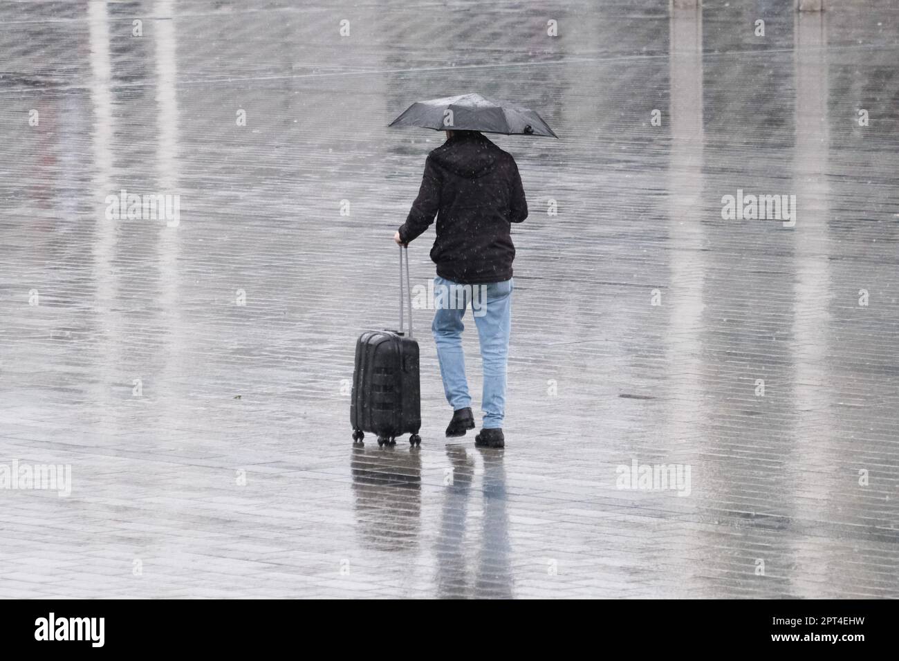 Gros plan homme tenant un parapluie sous la pluie et a une valise qui marche à l'arrière et pas de visage et de réflexion sur le sol. Vacances de pluie concept d'automne. Banque D'Images