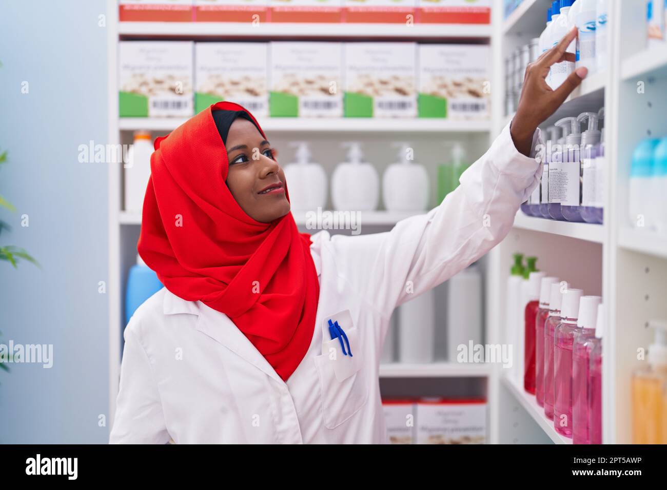 Jeune belle femme pharmacien souriant confiant tenant des médicaments sur des étagères à la pharmacie Banque D'Images