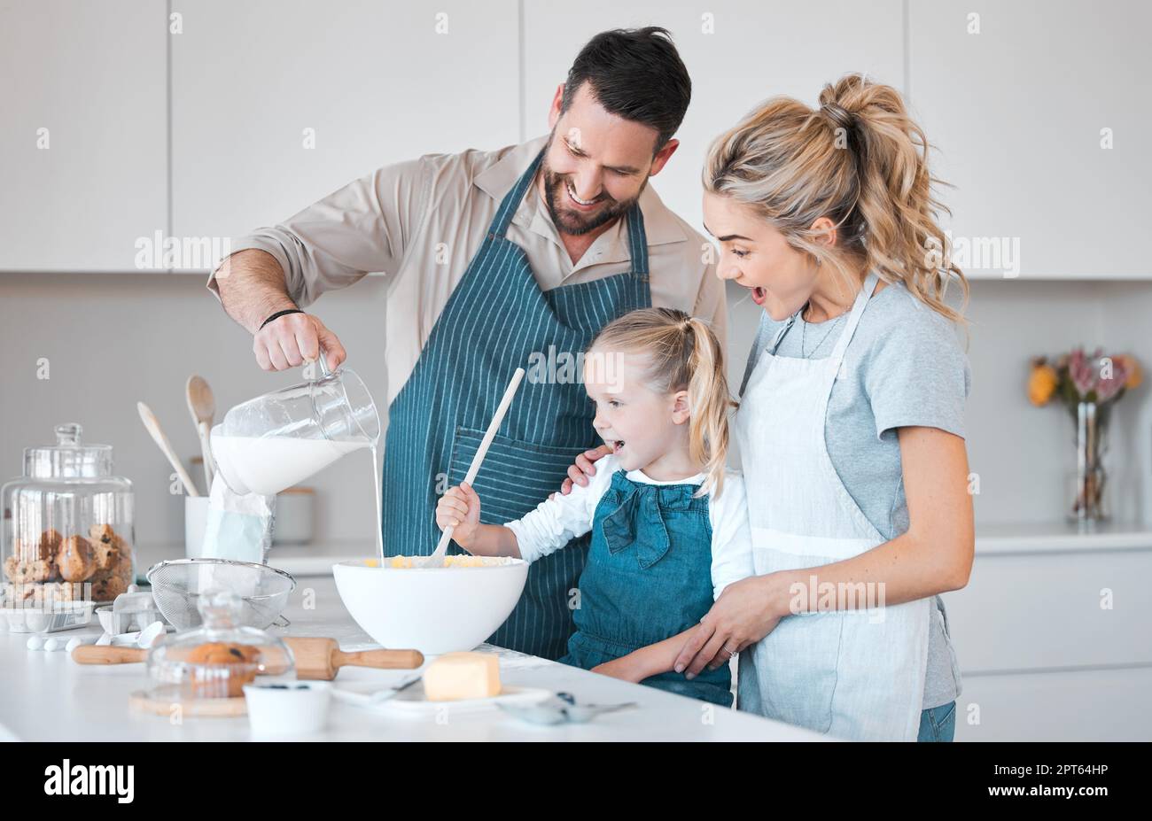 Père versant un pot de lait dans la pâte. Joyeux père cuisant avec sa fille. Famille caucasienne se cuisant ensemble.parents souriants aidant leur enfant Banque D'Images