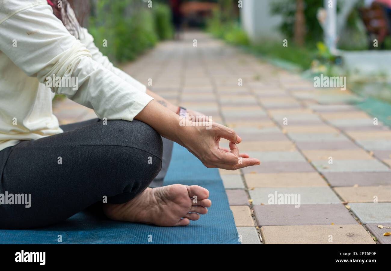 Gros plan femme mudra main geste faisant yoga détente en position lotus assis sur le tapis. À l'extérieur. Pratiquer la méditation dans la nature. Photo d'arrière-plan. Banque D'Images