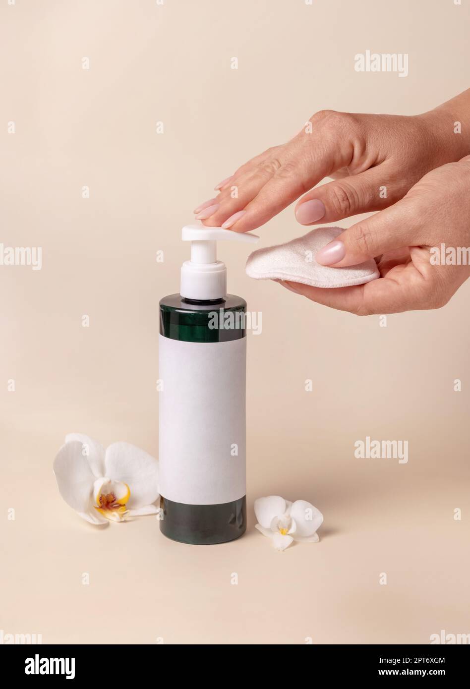 Une femme pompe à la main du liquide sur un tampon démaquillant d'une bouteille cosmétique près des fleurs d'orchidées sur beige gros plan, maquette d'étiquette. Produit de beauté pour les soins de la peau Banque D'Images