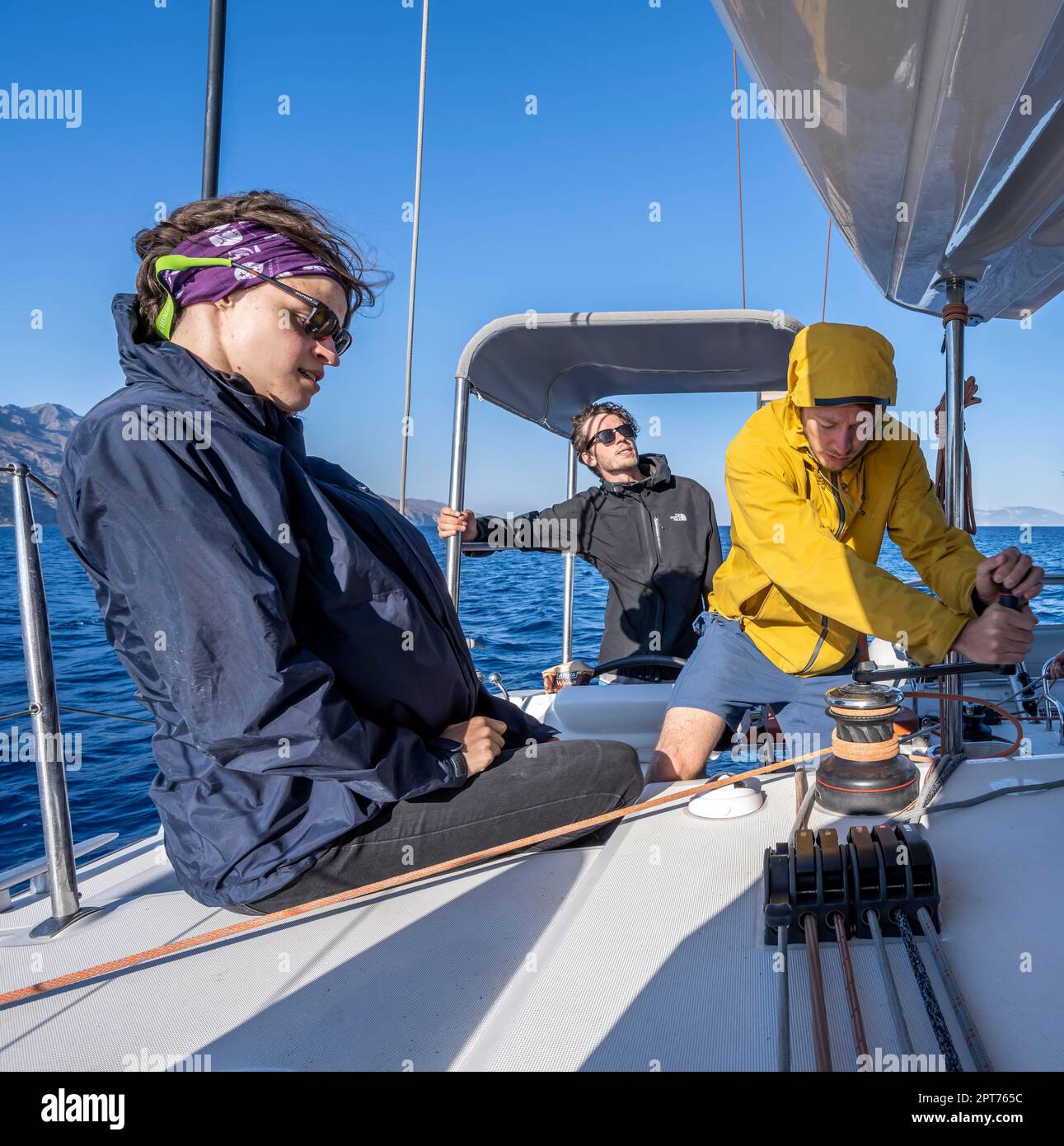 Marin utilisant un treuil avec bouchon de chantier naval, jeune femme et deux jeunes hommes naviguant, naviguant sur un catamaran de voile, Dodécanèse, Grèce Banque D'Images
