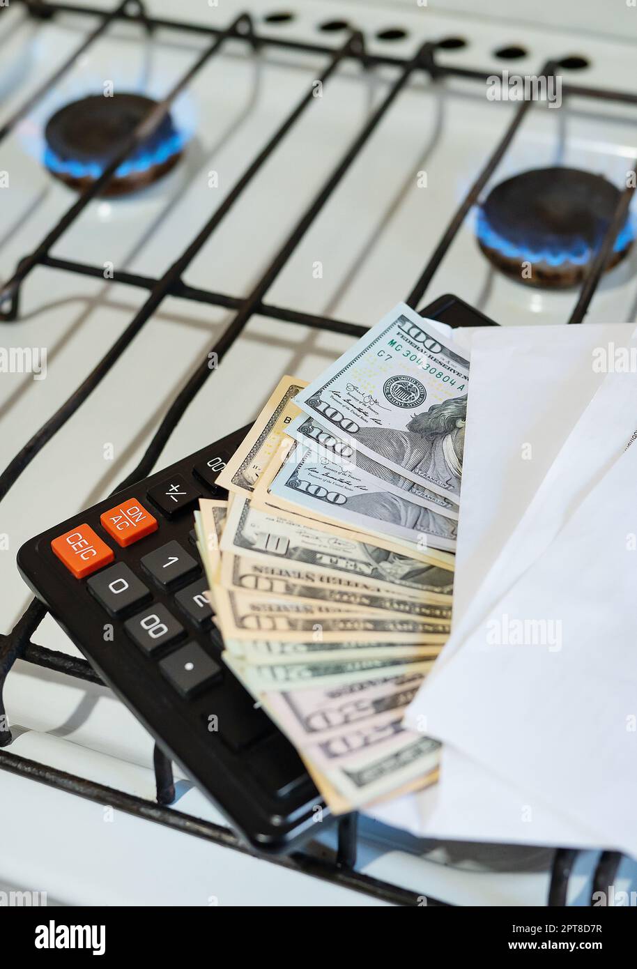 Paiement des factures de services publics, calculs sur une calculatrice. Les billets d'euro et de dollar sont près d'un brûleur à gaz en feu. Le concept d'augmenter le coût de nat Banque D'Images