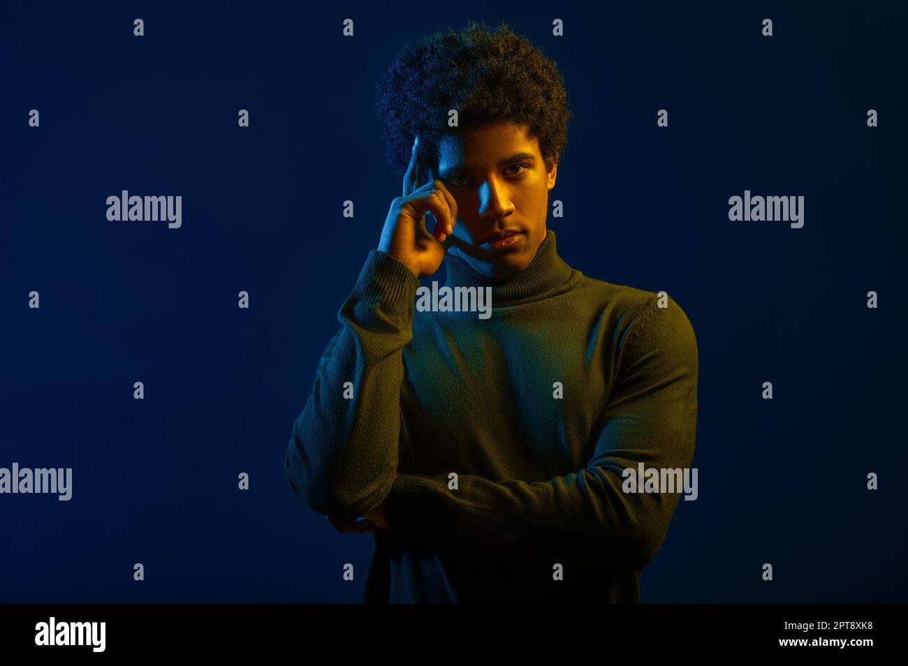 Portrait d'un jeune homme pensant tenir le doigt sur le temple sur fond sombre de studio Banque D'Images