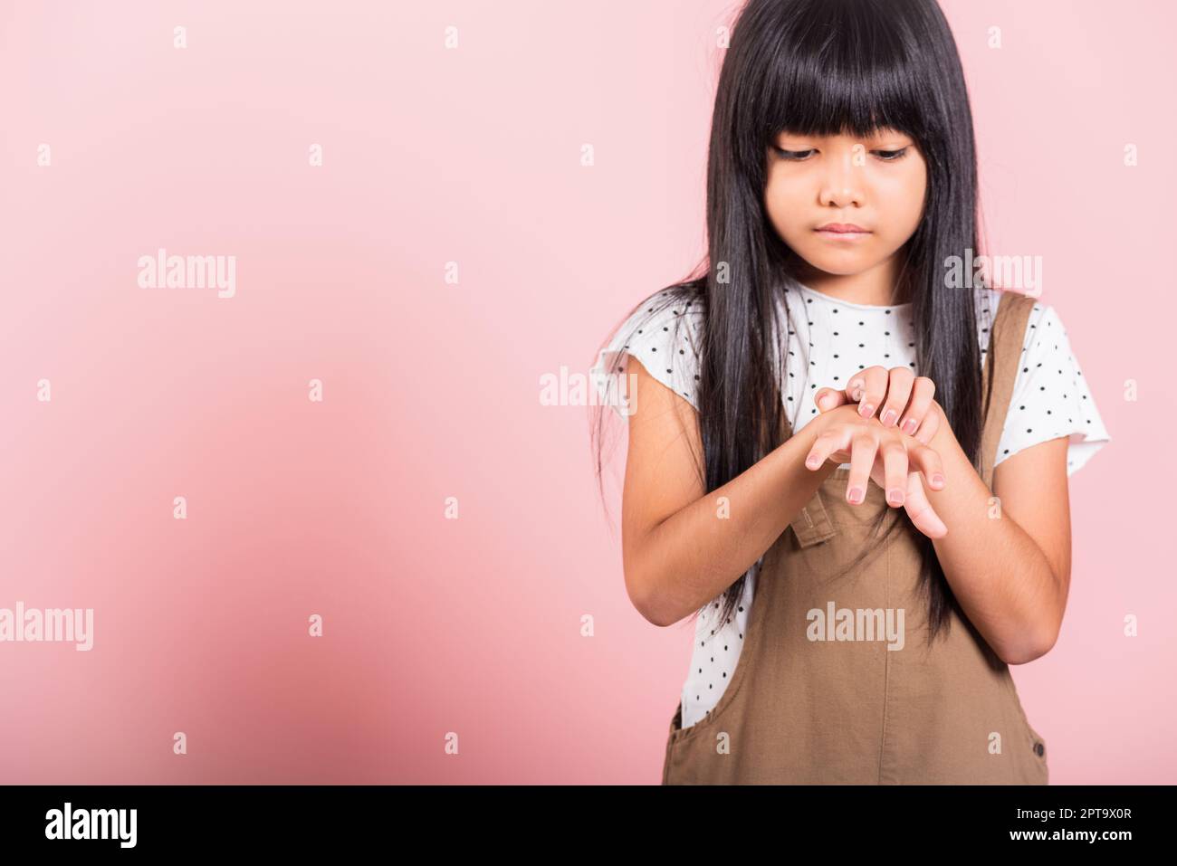 Petit enfant asiatique de 10 ans qui se gratte la main arrière de la piqûre de moustique au studio de tir isolé sur fond rose, dermatite de fille d'enfant et scabi Banque D'Images