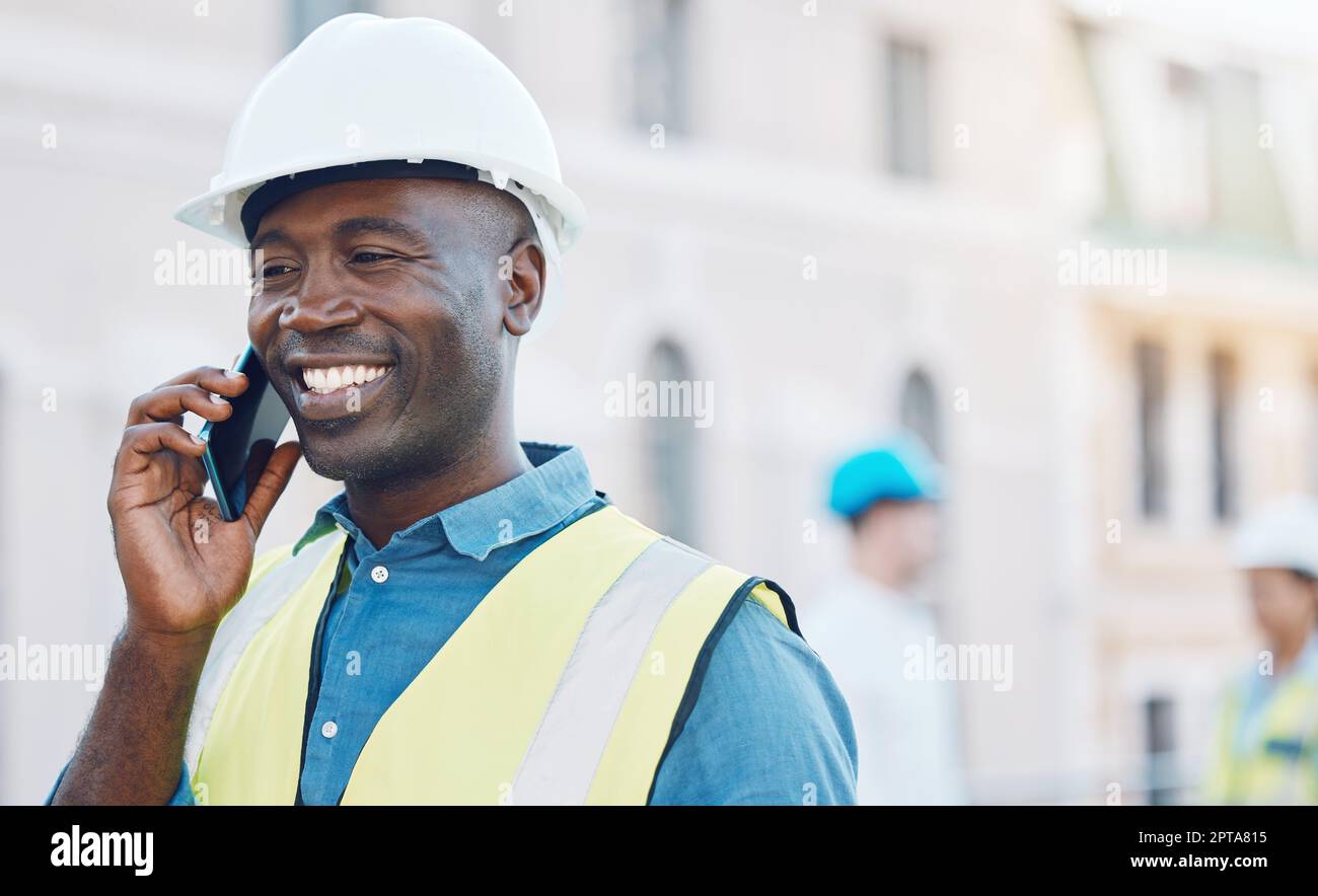 Travailleur de la construction utilisant un smartphone pour un appel téléphonique sur site. Portrait d'homme d'affaires heureux, souriant et noir dans un casque de sécurité et un équipement de sécurité sur le Th Banque D'Images