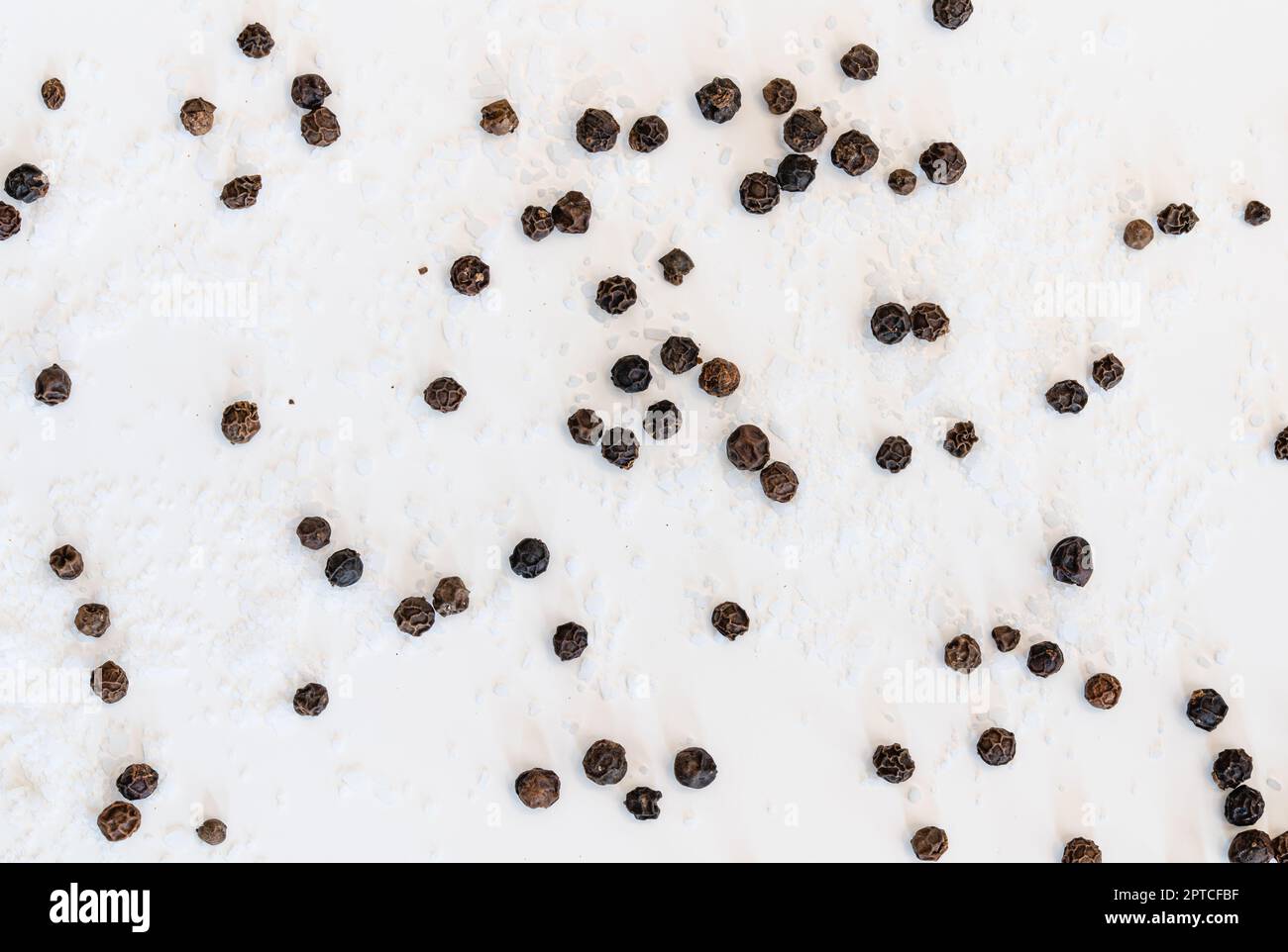 Sel de table et grains de poivre noir dispersés sur un fond blanc Banque D'Images