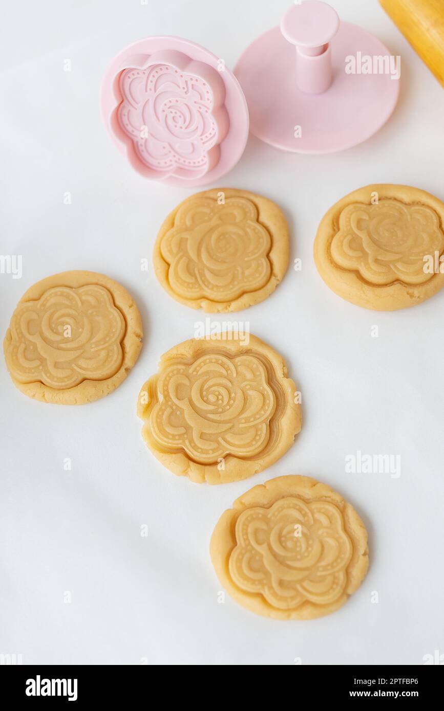 Le processus de fabrication de biscuits avec des formes sous forme de  fleurs, une broche roulante et une plaque de cuisson - des biscuits  prêts-à-faire avec une empreinte de la forme Photo
