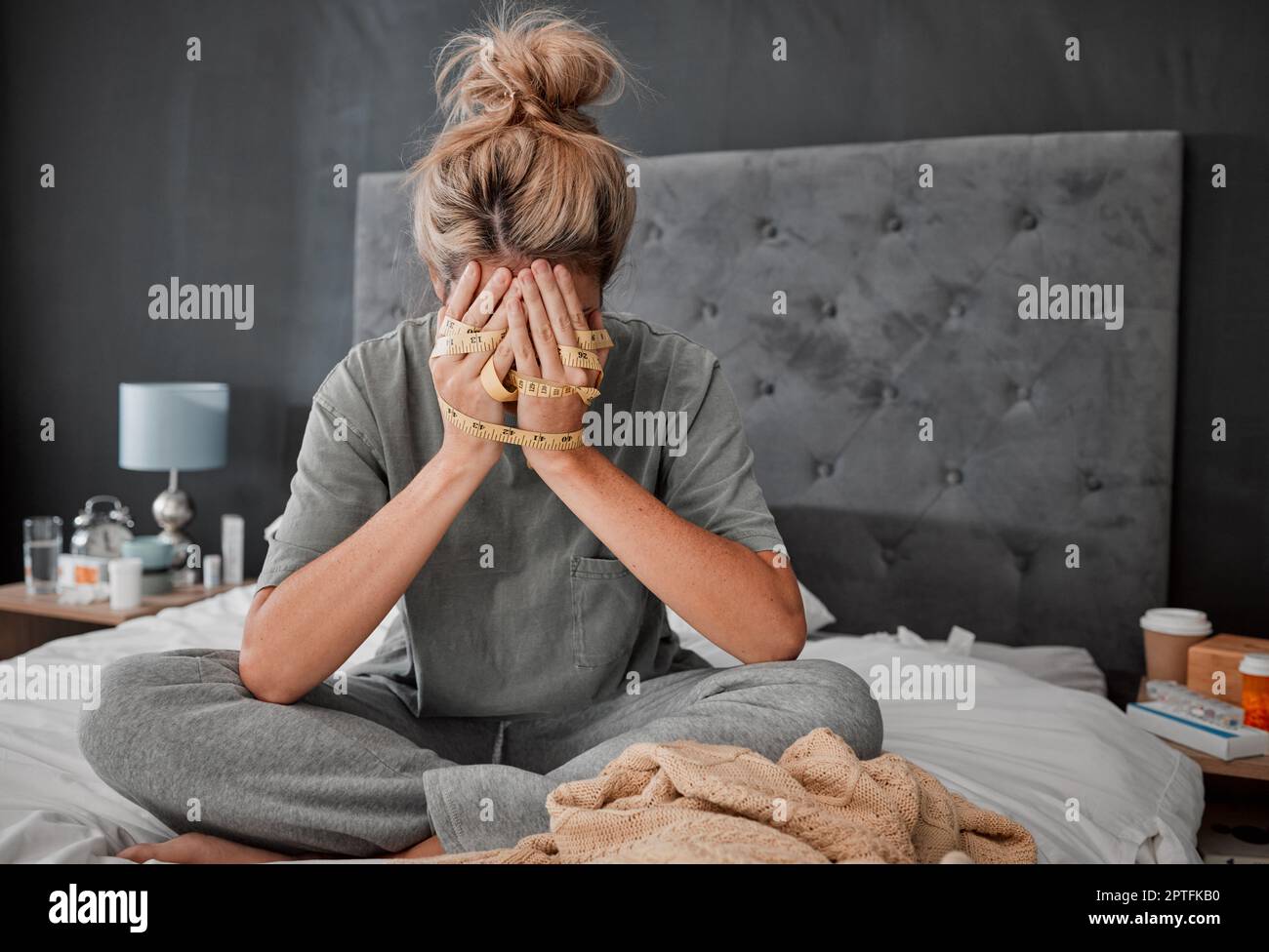 Les mains, l'anorexie et la dépression avec une femme sur son lit tenant un  mètre ruban et regardant triste ou frustré. La santé mentale, la boulimie  et la démorde alimentaire Photo Stock -