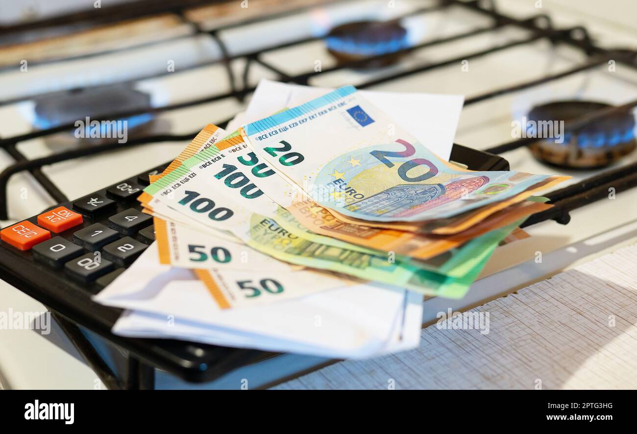 Paiement des factures de services publics, calculs sur une calculatrice. Les billets d'euro et de dollar sont près d'un brûleur à gaz en feu. Le concept d'augmenter le coût de nat Banque D'Images