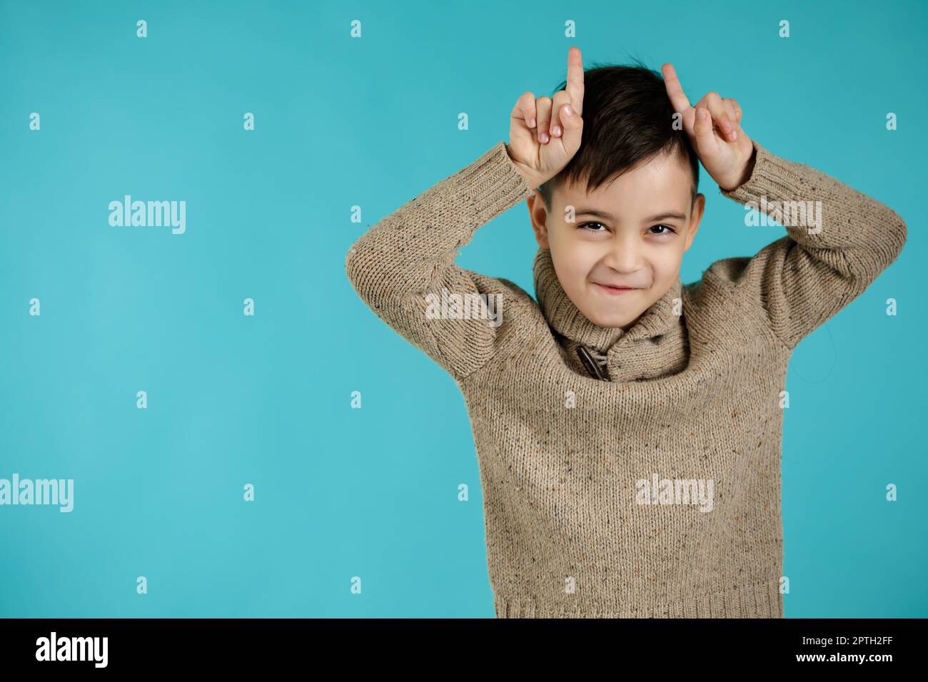 joyeux petit garçon drôle de faire un geste drôle avec le doigt sur la tête comme des cornes de taureau sur fond bleu. expression faciale Banque D'Images