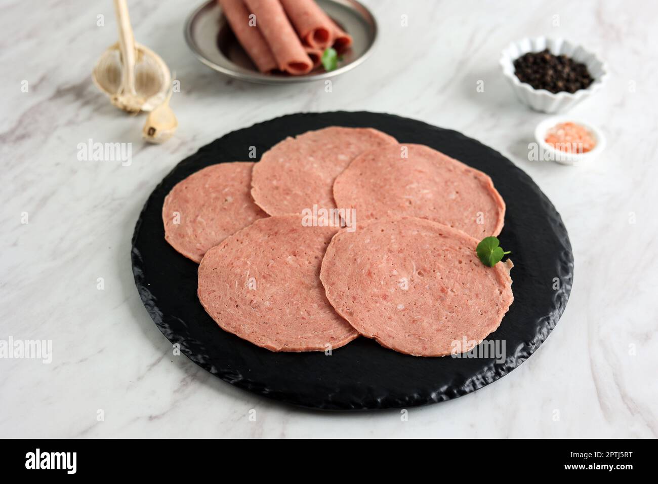 Tranches de saucisse fumées, saucisse finement coupée, prêtes à cuire. Salami de bœuf sur l'assiette noire Banque D'Images