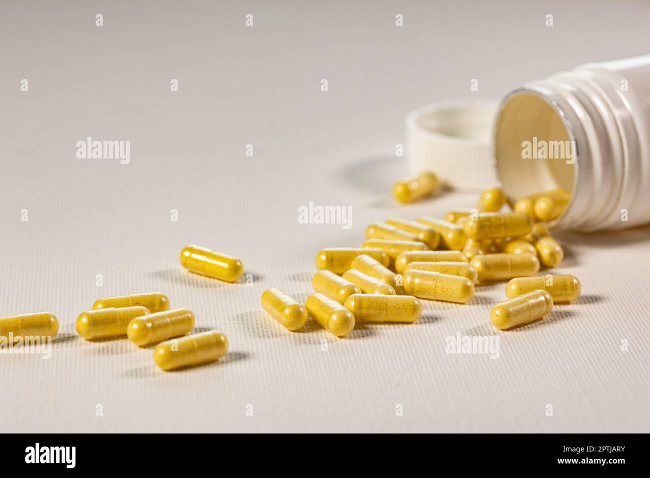 Pilules jaunes pour usage oral sur fond blanc. Médicaments sous forme de comprimés dans un pot en plastique blanc. Concept de soins de santé et de médecine Banque D'Images