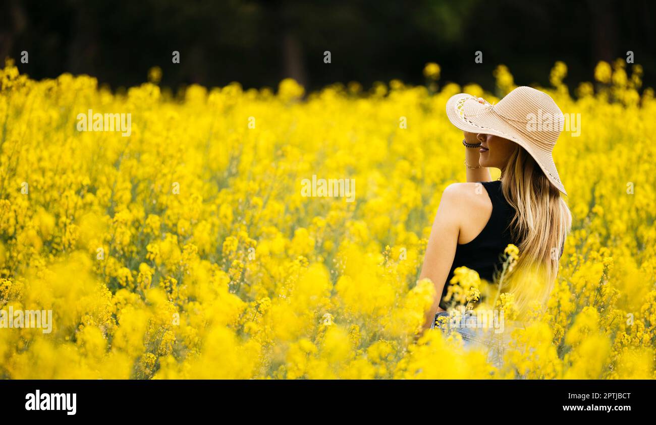 Belle fille aux cheveux blone pose au milieu d'un champ de fleurs de colza jaune Banque D'Images