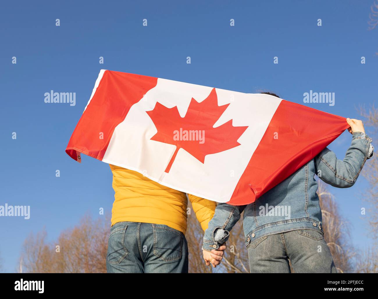 Un homme et une femme méconnaissables, tenant les mains, sont debout avec un grand drapeau canadien derrière leur dos contre le ciel Banque D'Images