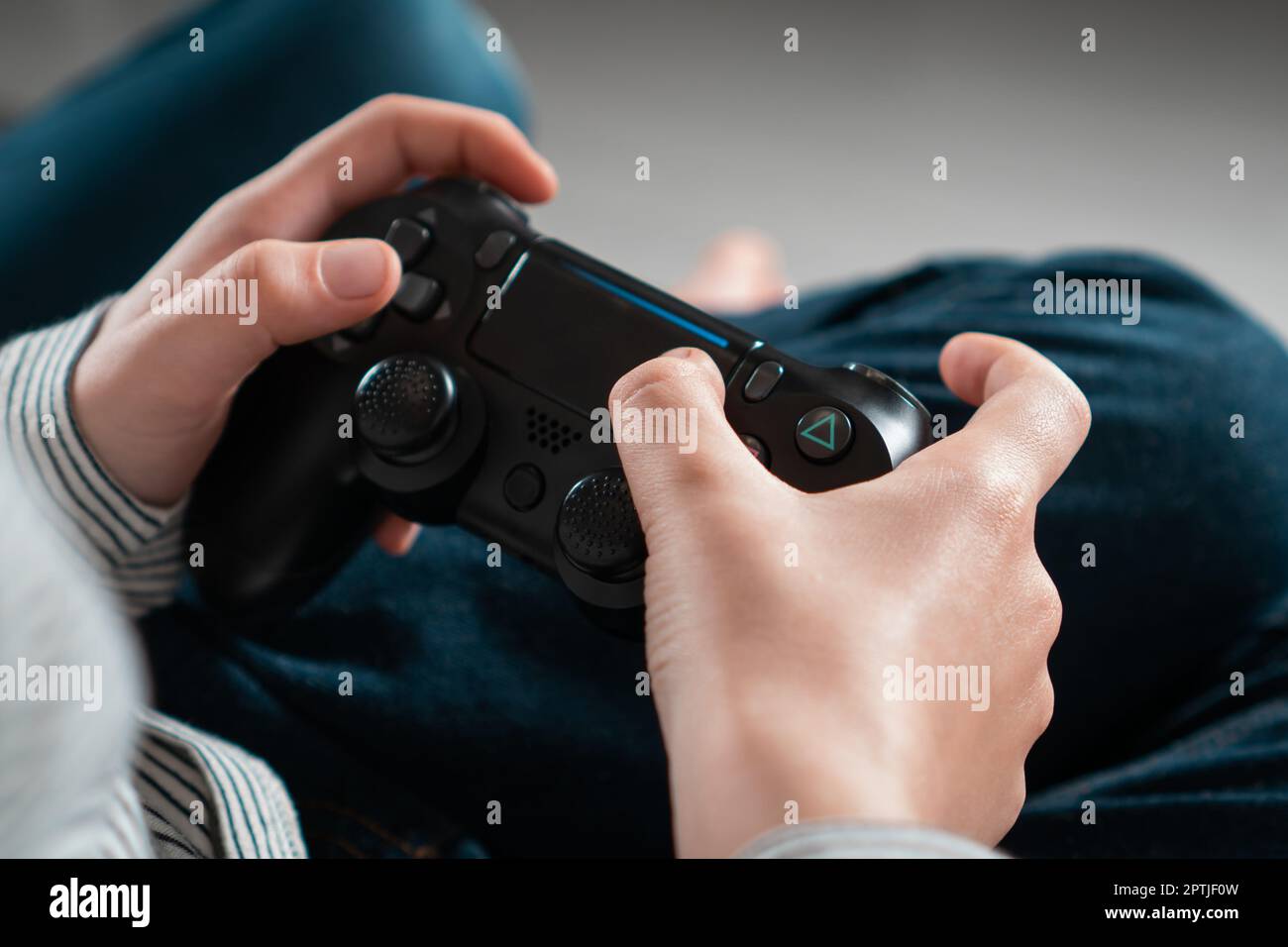 Enfant adolescent méconnaissable assis à la maison, tenant une manette de jeu noire, jouant à des jeux vidéo sur la console