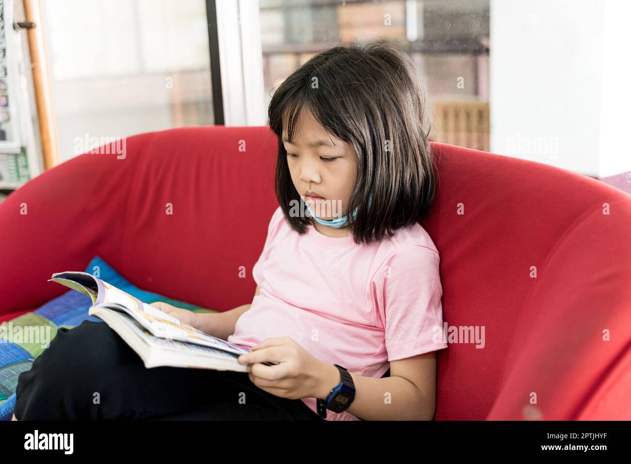 Petite fille asiatique est en train de lire un livre tout en étant assis près de la fenêtre Banque D'Images