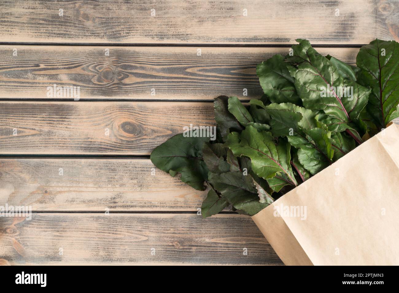 Feuillage vert luxuriant et tiges de racines de betteraves se cachant dans un sac écologique, emballage sur fond de bois. Achats écologiques, livraison de nourriture et légumes de ferme bio Banque D'Images