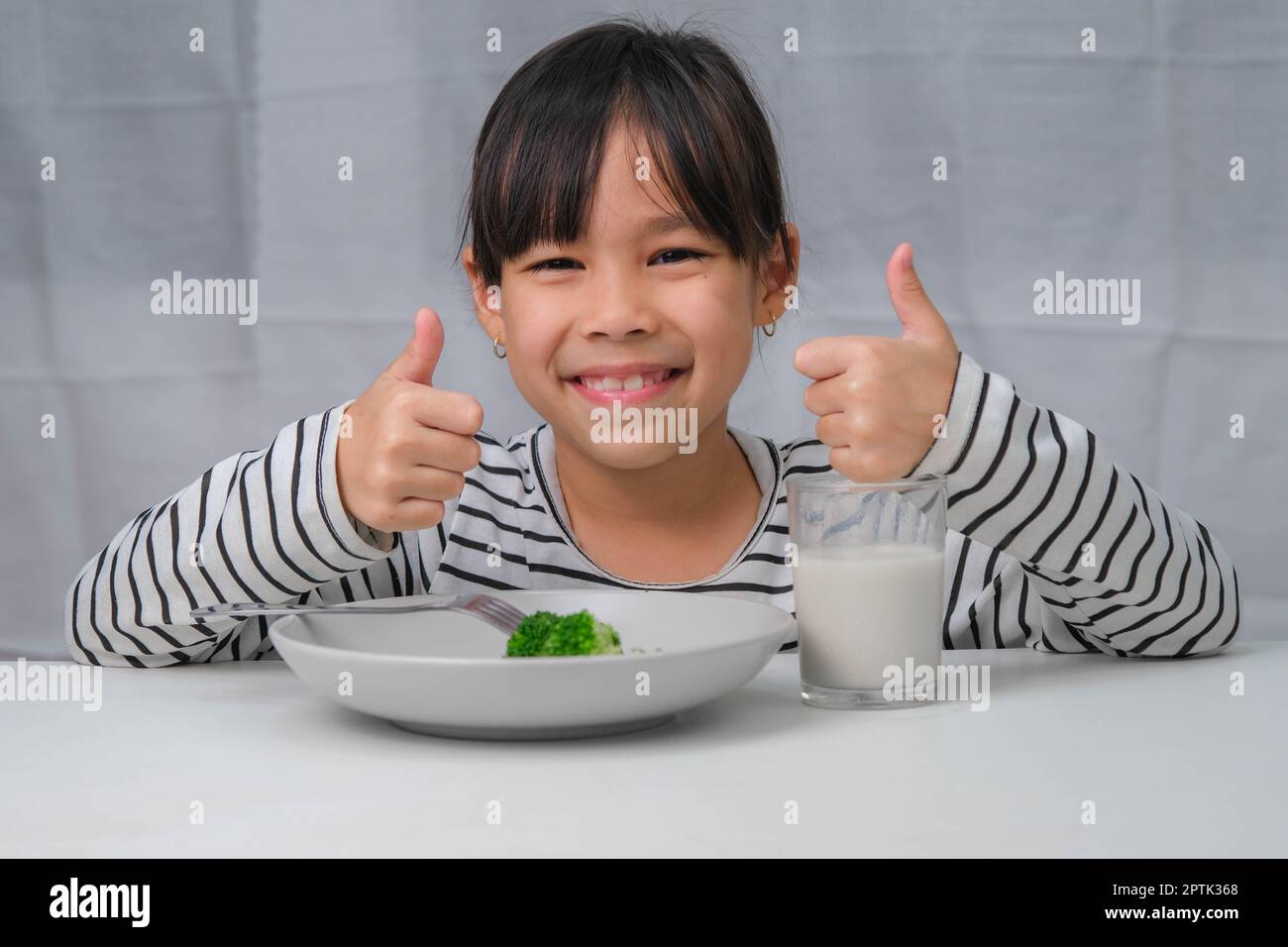 Jolie fille asiatique buvant un verre de lait le matin avant d'aller à l'école. La petite fille mange des légumes sains et du lait pour ses repas. Santé FO Banque D'Images